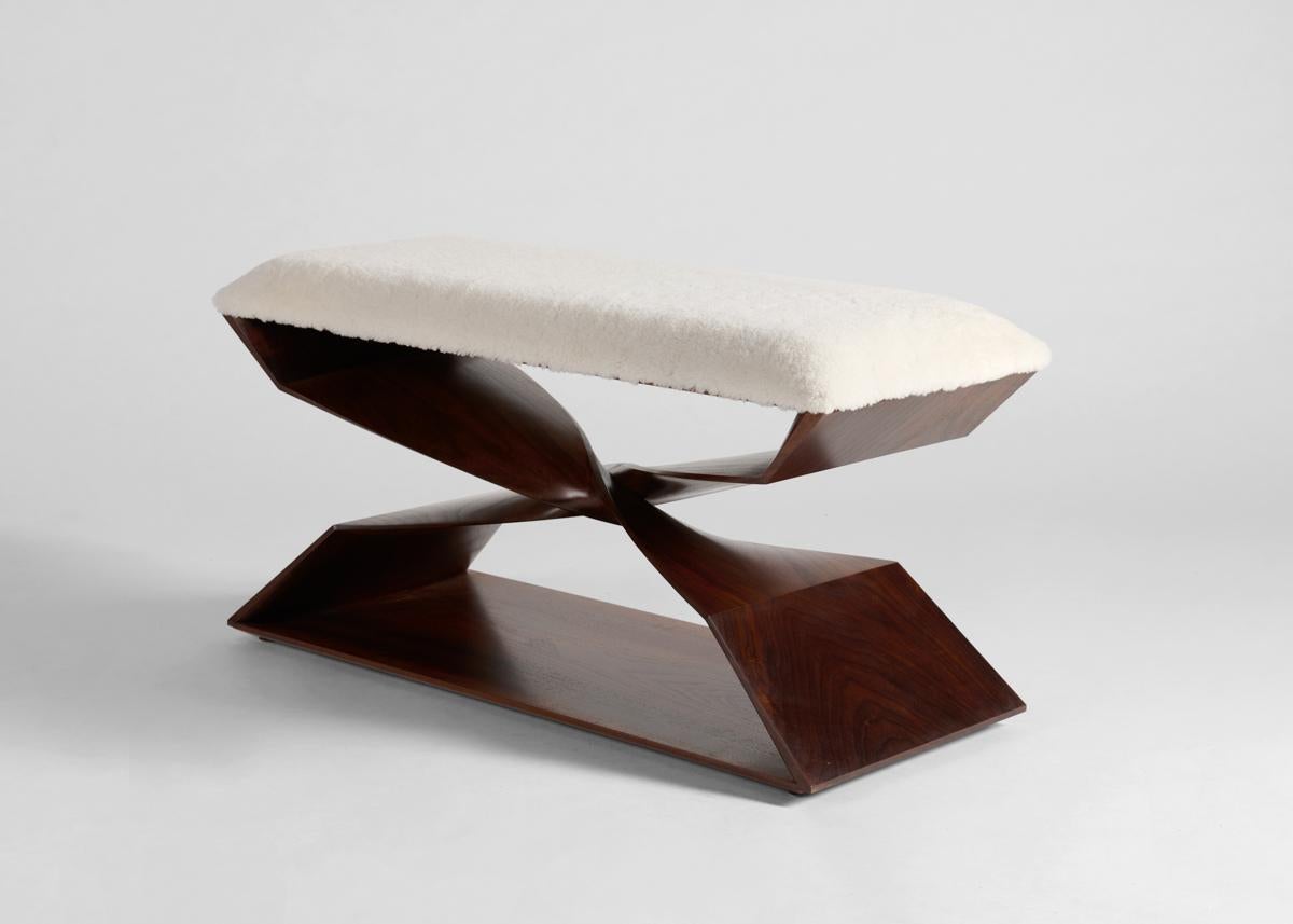 This sculptural hand-carved bench is part of a line of contemporary furniture designed by blending digital technology with fine traditional craftsmanship. Carved of American Walnut, the stool features a crisscrossing buttress, which, twisting 180