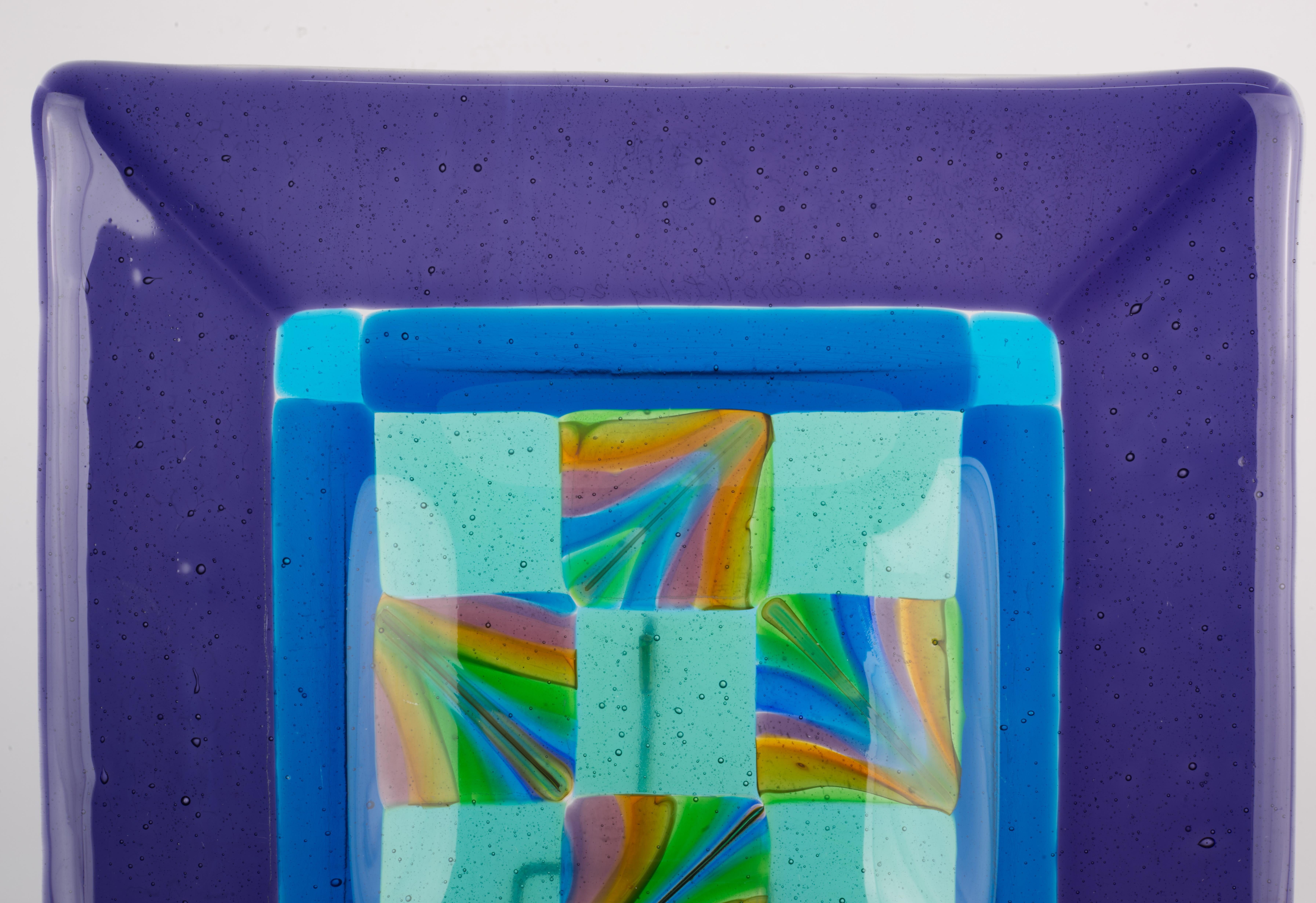  Fused glass square vide-poche or ashtray has wide rim of deep amethyst purple color and complex central bowl with checkered pattern in the center, encircled by a blue band. All areas of solid color glass have controlled bubbles effect, adding to