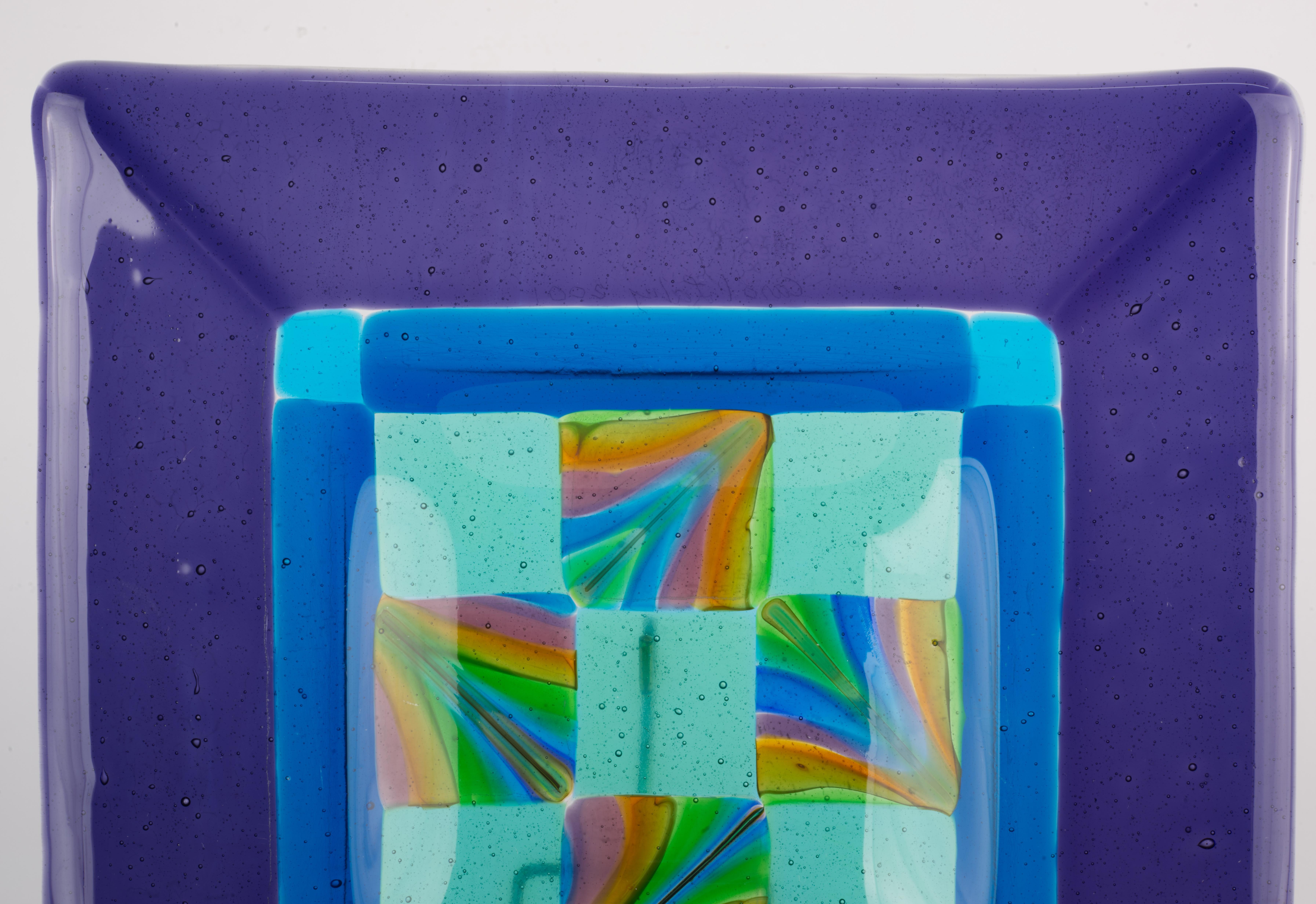  El vide-poche o cenicero cuadrado de vidrio fundido tiene el borde ancho de color púrpura amatista intenso y un cuenco central complejo con un dibujo a cuadros en el centro, rodeado por una banda azul. Todas las zonas de vidrio de color sólido