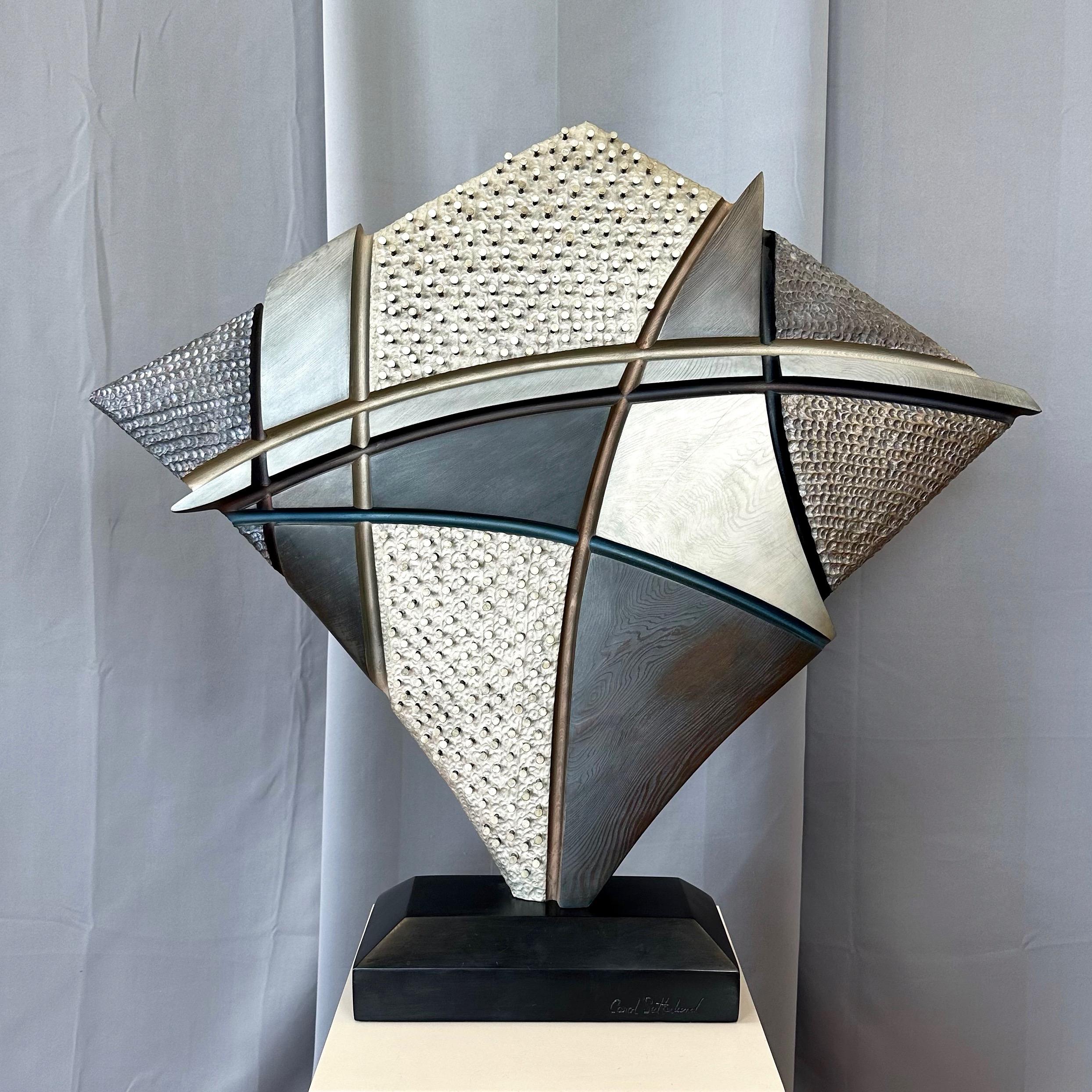 A large 1980s abstract mixed-media wood sculpture titled “Martyr’s Shield” by notable Northern California artist Carol Setterlund.

Hand-carved from a single piece of solid redwood with various geometric forms, textures, and intersecting lines