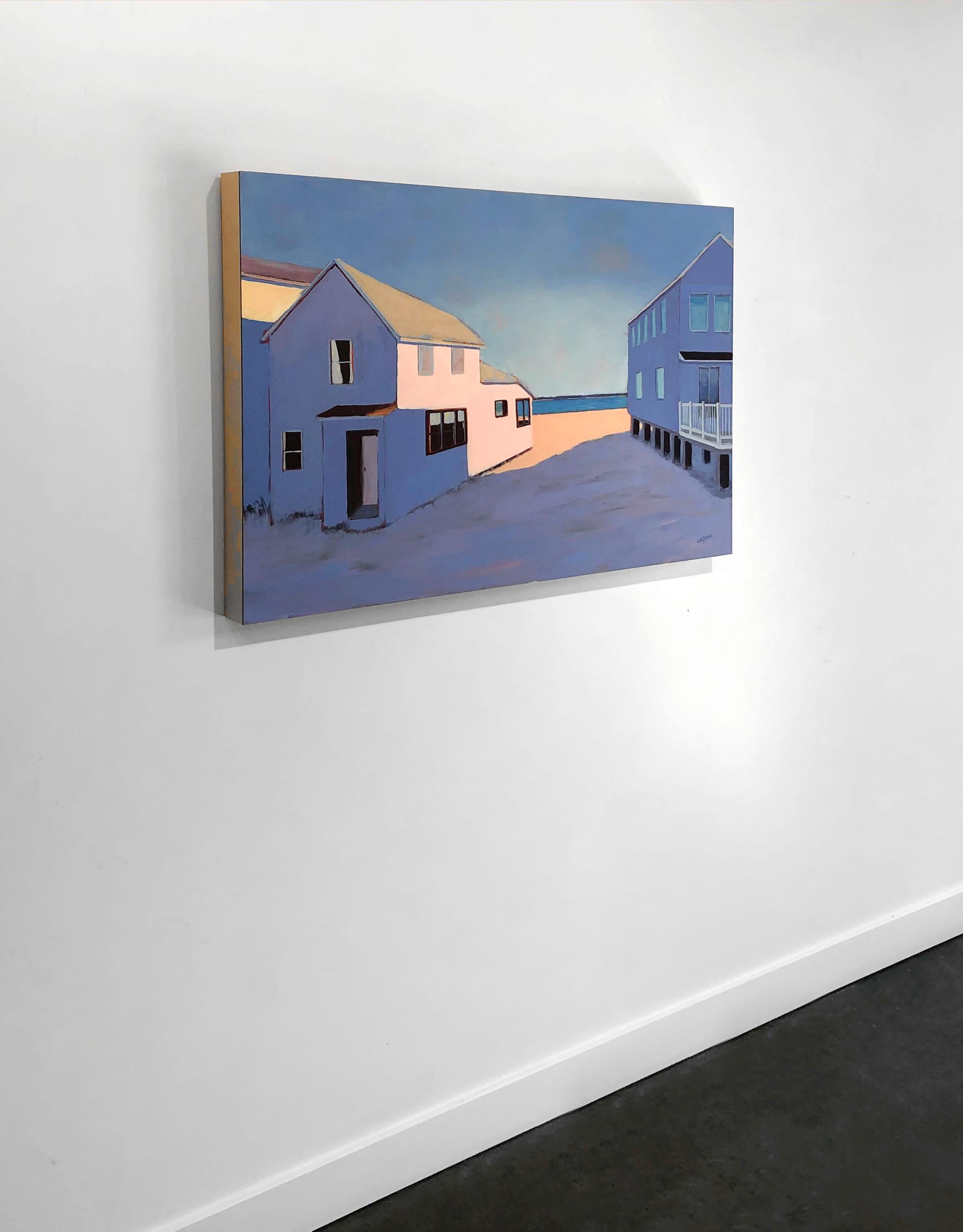 This contemporary landscape painting by Carol Young depicts two beach house-like buildings, with a sandy walkway in between that leads to a body of water. The two buildings and most of the sand is in shade, which the artist has rendered as an almost