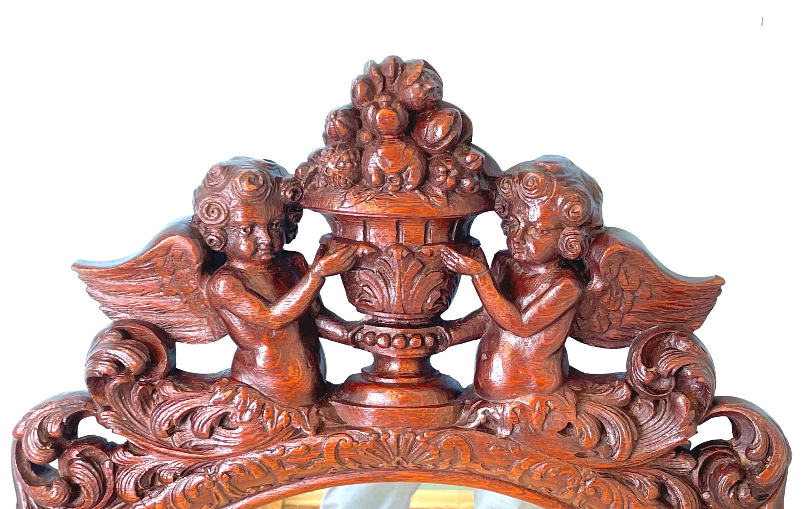 n Extremely Attractive And Very Good Quality Late 19th Century Oak Oval Wall Mirror, In The Carolean Style, Having Foliate Carved Cushion Frame Surmounted By Pair Of Carved Cherubs Holding Central Set Urn With Overflowing Carved Fruit. 

This Late