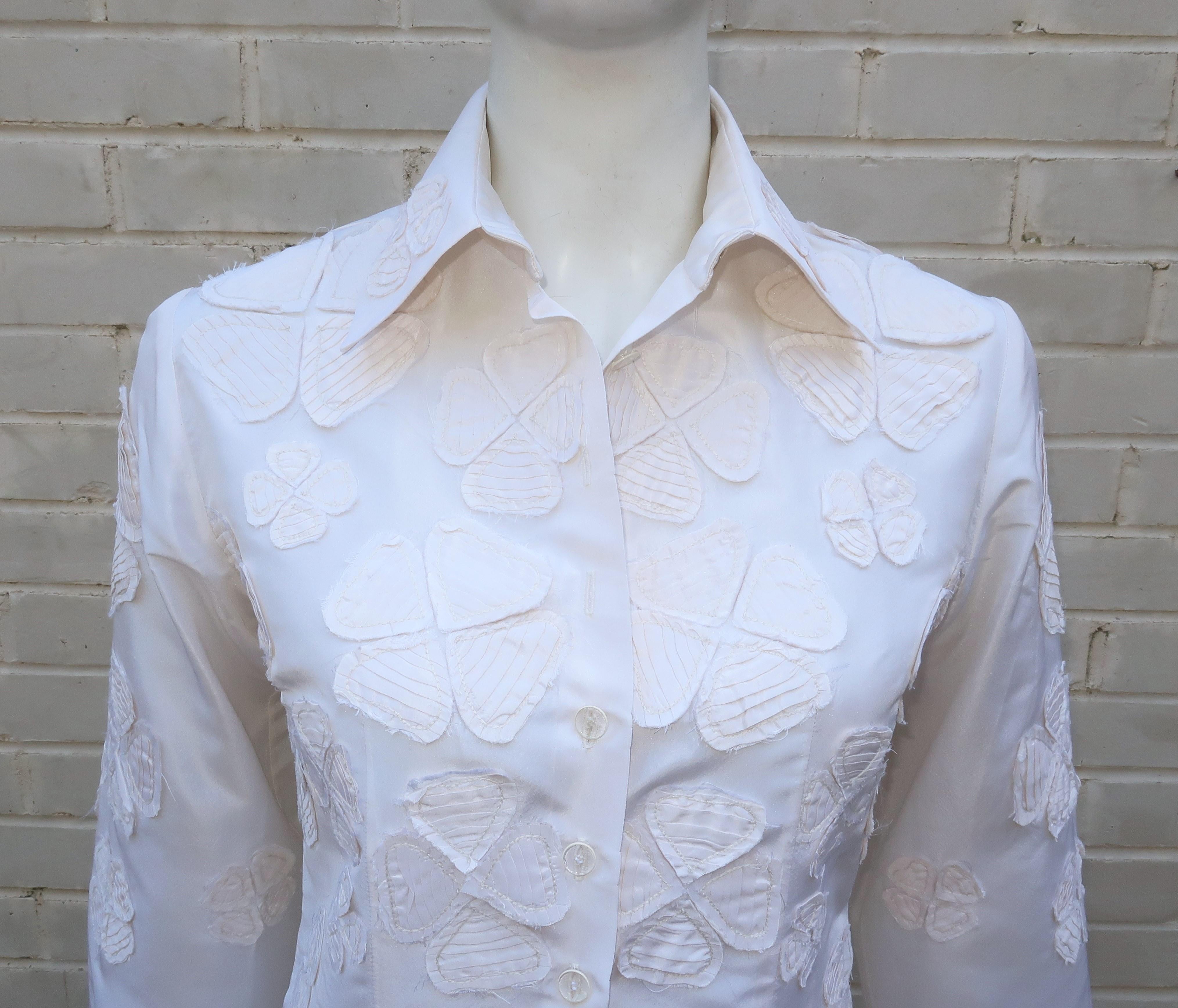 A beautiful crisp white blouse is the signature look for ultra stylish designer, Carolina Herrera.  This blouse features a candlelight white silk taffeta covered in four leaf clover style appliques layered with deconstructed edges.  It buttons at