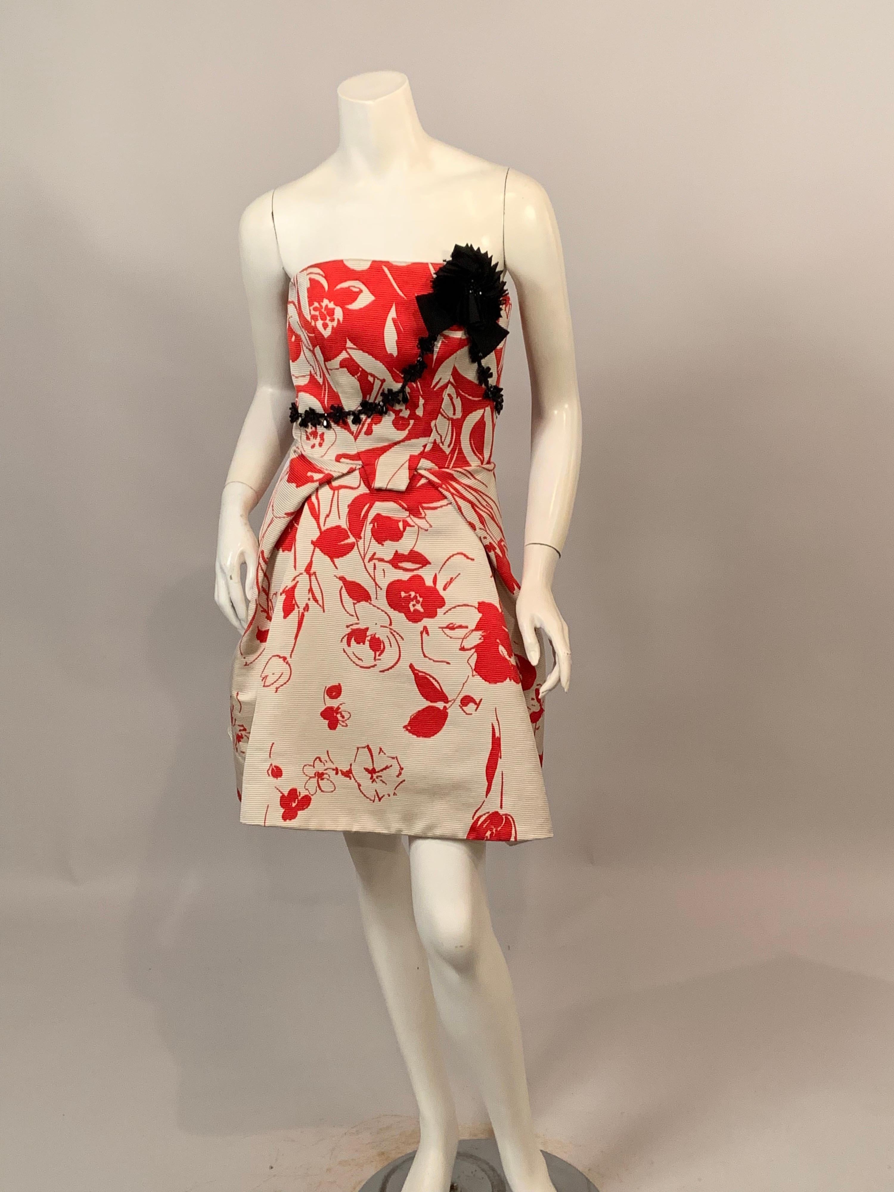 A bright red floral pattern on a cream ribbed silk ottoman is used for this chic strapless evening dress from Carolina Herrera. The bodice is decorated with black silk ribbon and jet beadwork. The dress has a center back zipper, two generous pockets