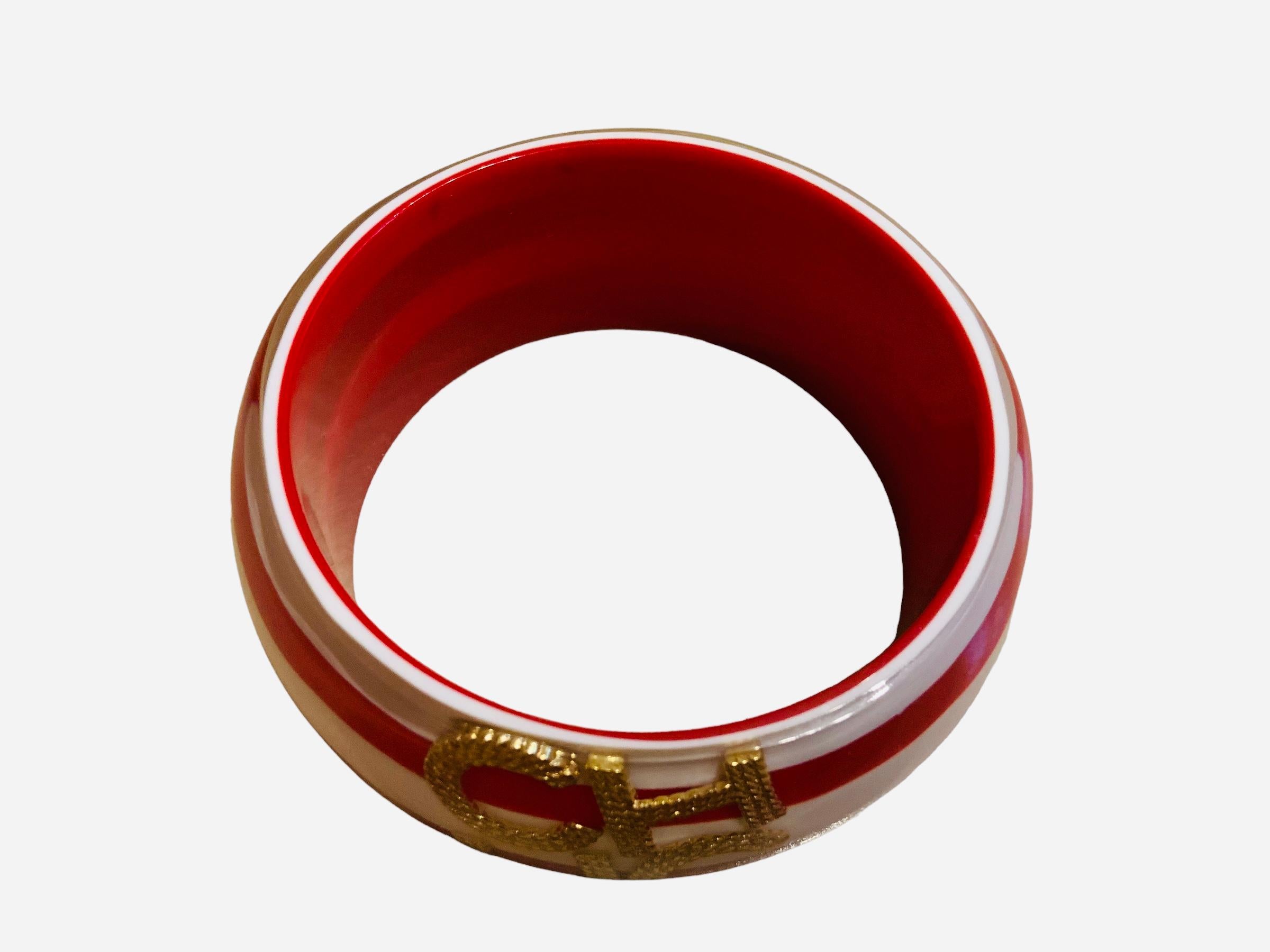 This is a Carolina Herrera red and white resin bangle. It depicts a red and white “peppermint starlights” pattern. It is adorned in the center with gold tone double upper case initials of CH from Carolina Herrera.