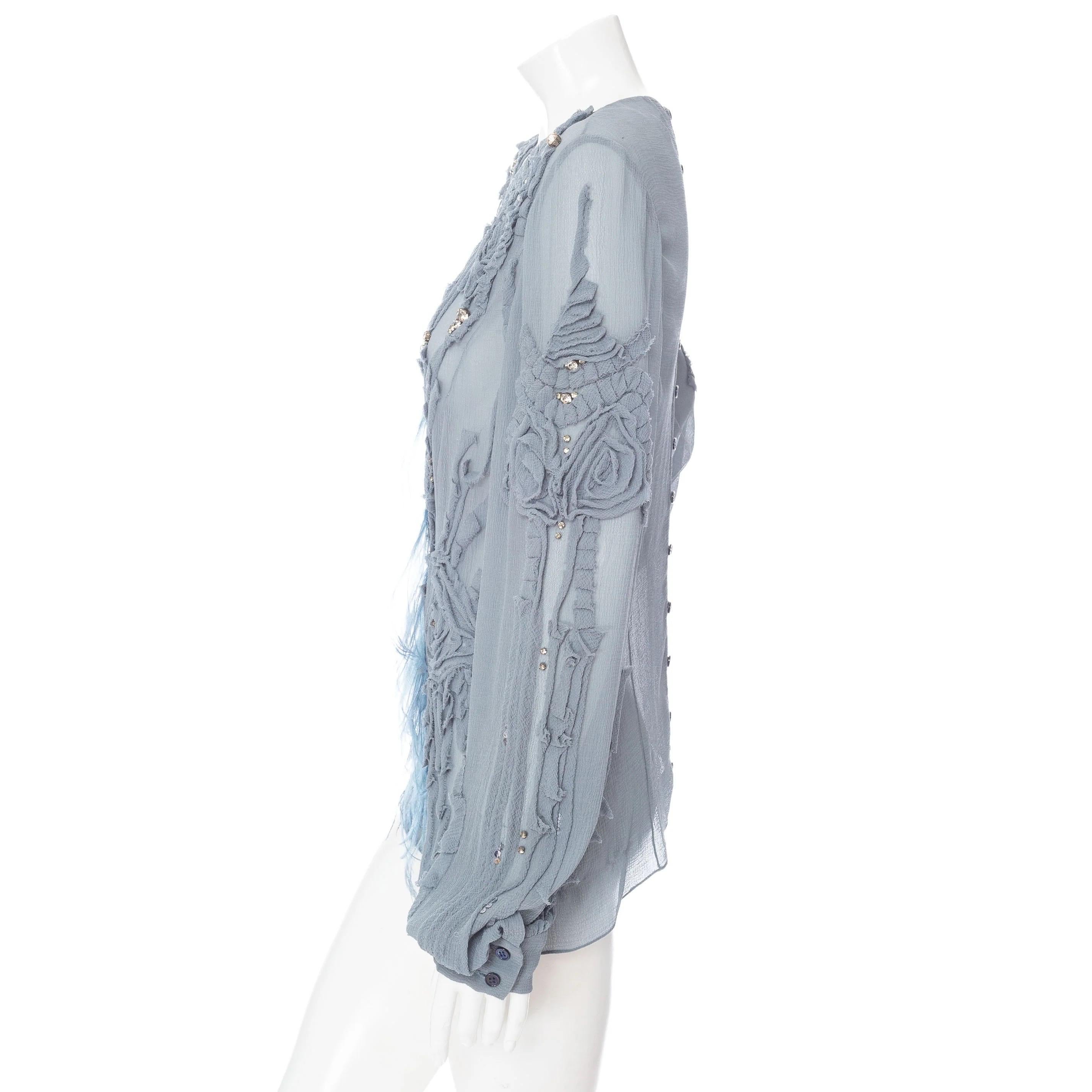 Carolina Herrera: camicetta semi trasparente con perline e piume, blu. 

Pronto per l'autunno 2008
Blu polvere
Semi trasparente
Manica lunga
Scollo rotondo
Rosetta applicata con bordi grezzi
Decorazioni con perline, cristalli e piume
Maniche a