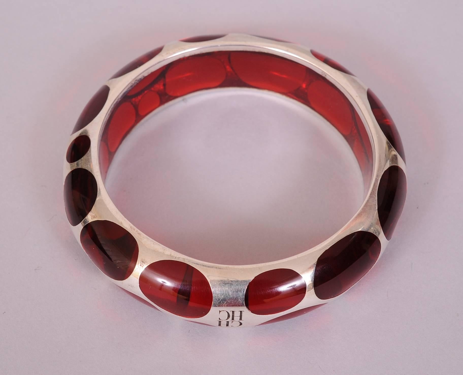 This Bangle bracelet is both stylish and fun. The play of sterling silver and red Lucite is quite witty. The negative space in the silver creates polka dots i a range of sizes. The bracelet is signed with the CH logo and it is in excellent