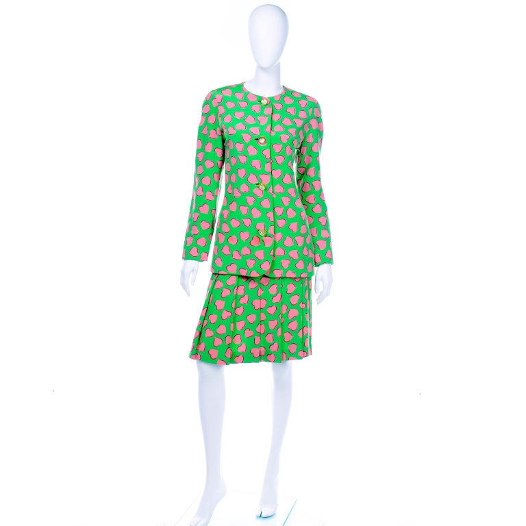 This amazing Carolina Herrera green silk skirt suit is in a pink heart novelty print. This great outfit would make a perfect day dress alternative! The collarless jacket  has rounded shoulders and long tapered sleeves. The jacket has darts along the