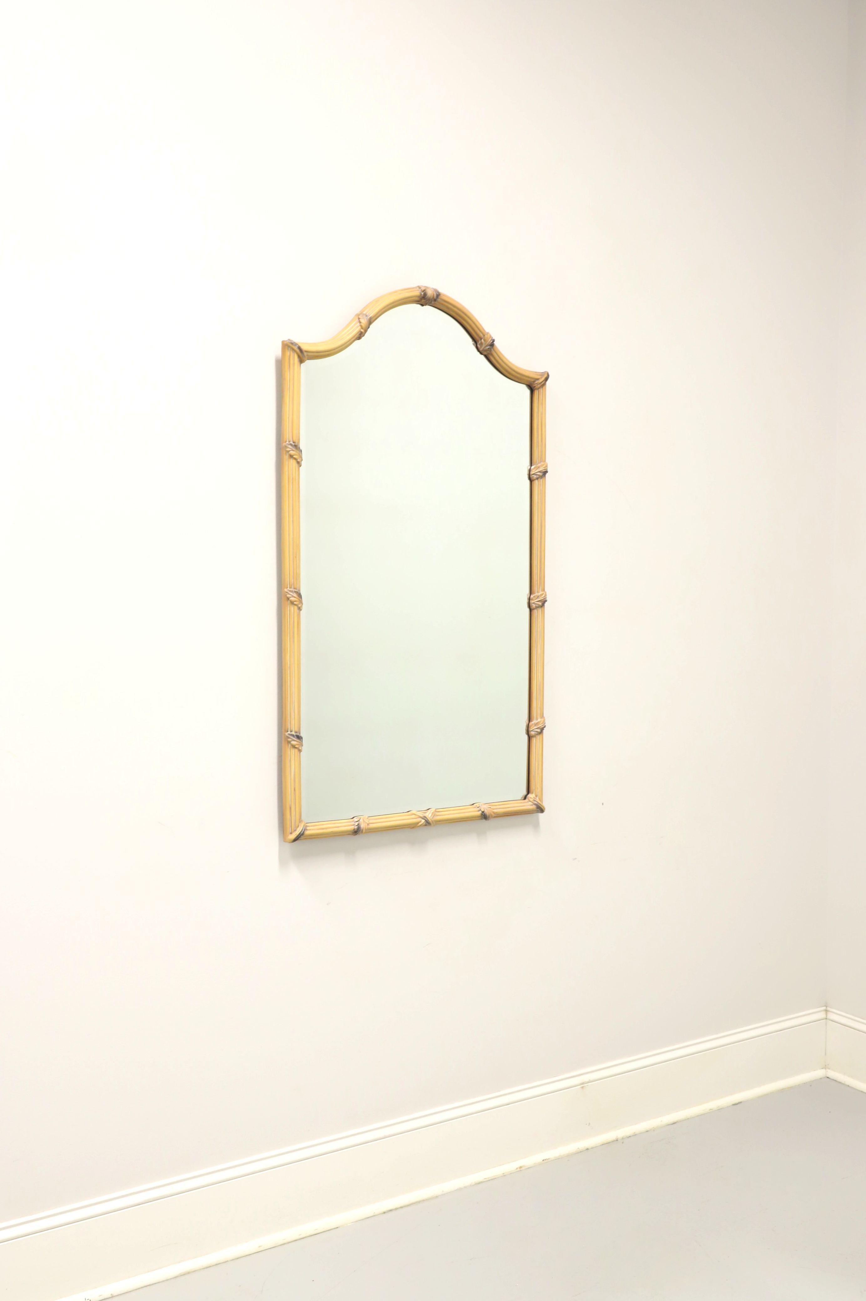 A French Country style wall mirror by Carolina mirror company. Beveled mirrored glass in a light colored faux bamboo frame with an arched top and decorative carved leaf accents. Made in North Carolina, USA, in the late 20th Century. 

Measures: