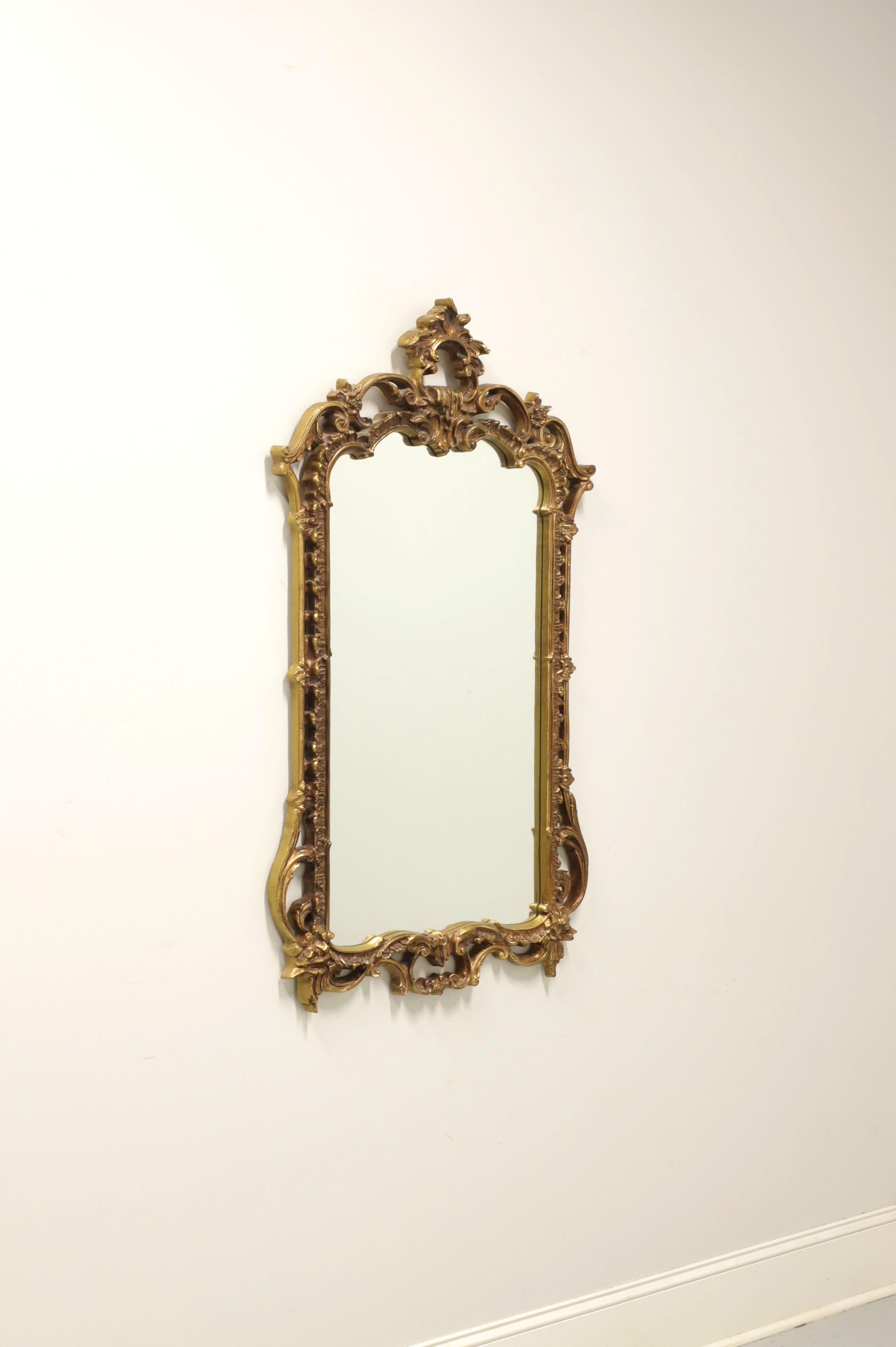 A Rococo style wall mirror by Carolina Mirror. Mirror glass in an intricately molded gold gilt painted composite frame with leaves to top center and floral accents throughout. Made in North Carolina, USA, in the late 20th Century.

Measures: 27.75w