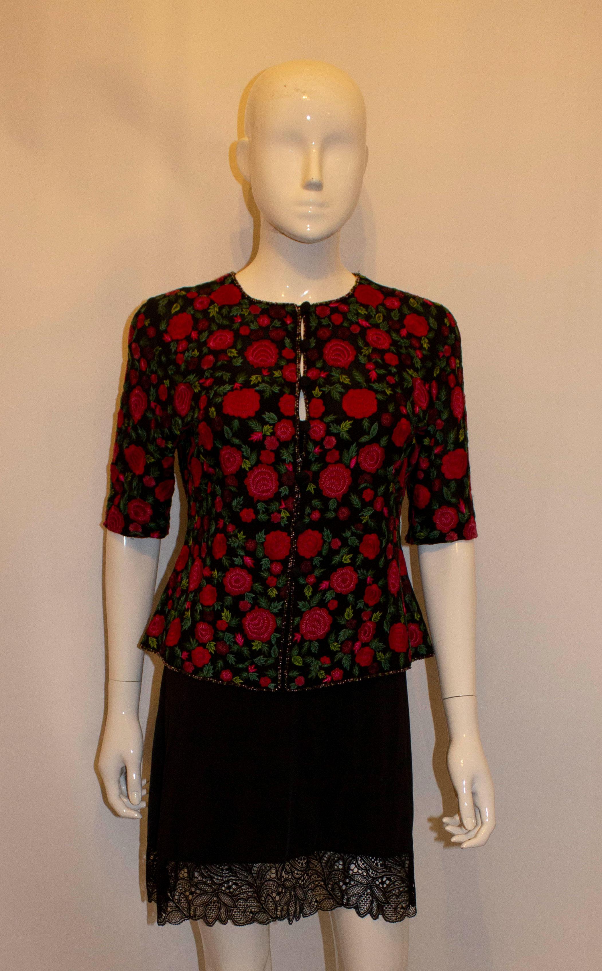 A pretty and easy to wear evening jacket/ top by Caroline Charles.  The jacket has a black background with multi colour edging and a button front opening. It has short leaves and a round neckline.  Measurements : Bust 37'' , length 21''