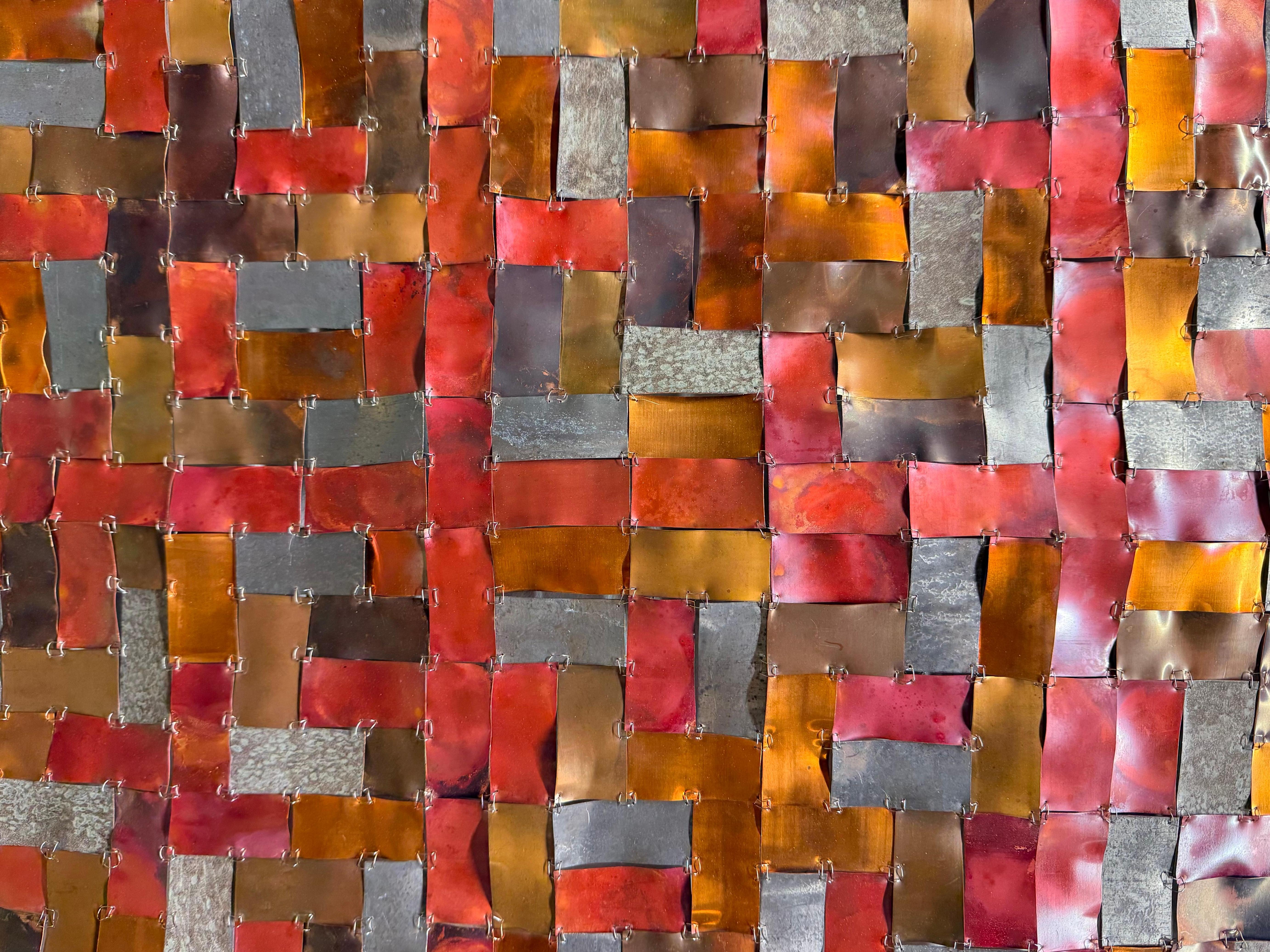 Remind Me is a striking mixed-metal composition by contemporary artist Carolyn Millstein, known for her innovative use of reclaimed materials. This piece features a grid of rectangular strips of copper and lead-coated copper roofing meticulously