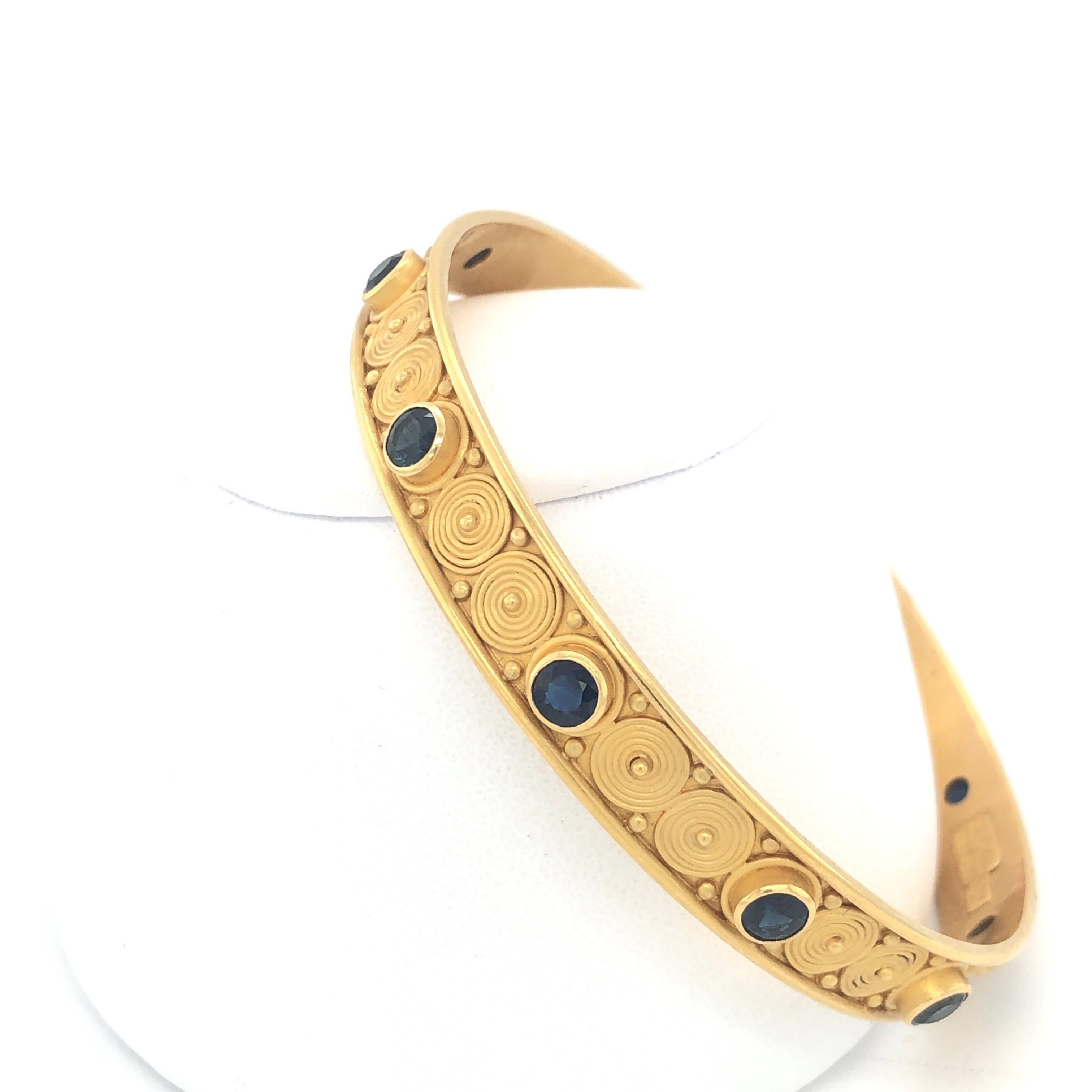 The unique artistry of Carolyn Tyler.  Beautiful Yellow Gold and Blue Sapphire Bangle with the classic detail work that she is famous for.  Stamped C Tyler and 18K Gold.  Size 8 inches. 
