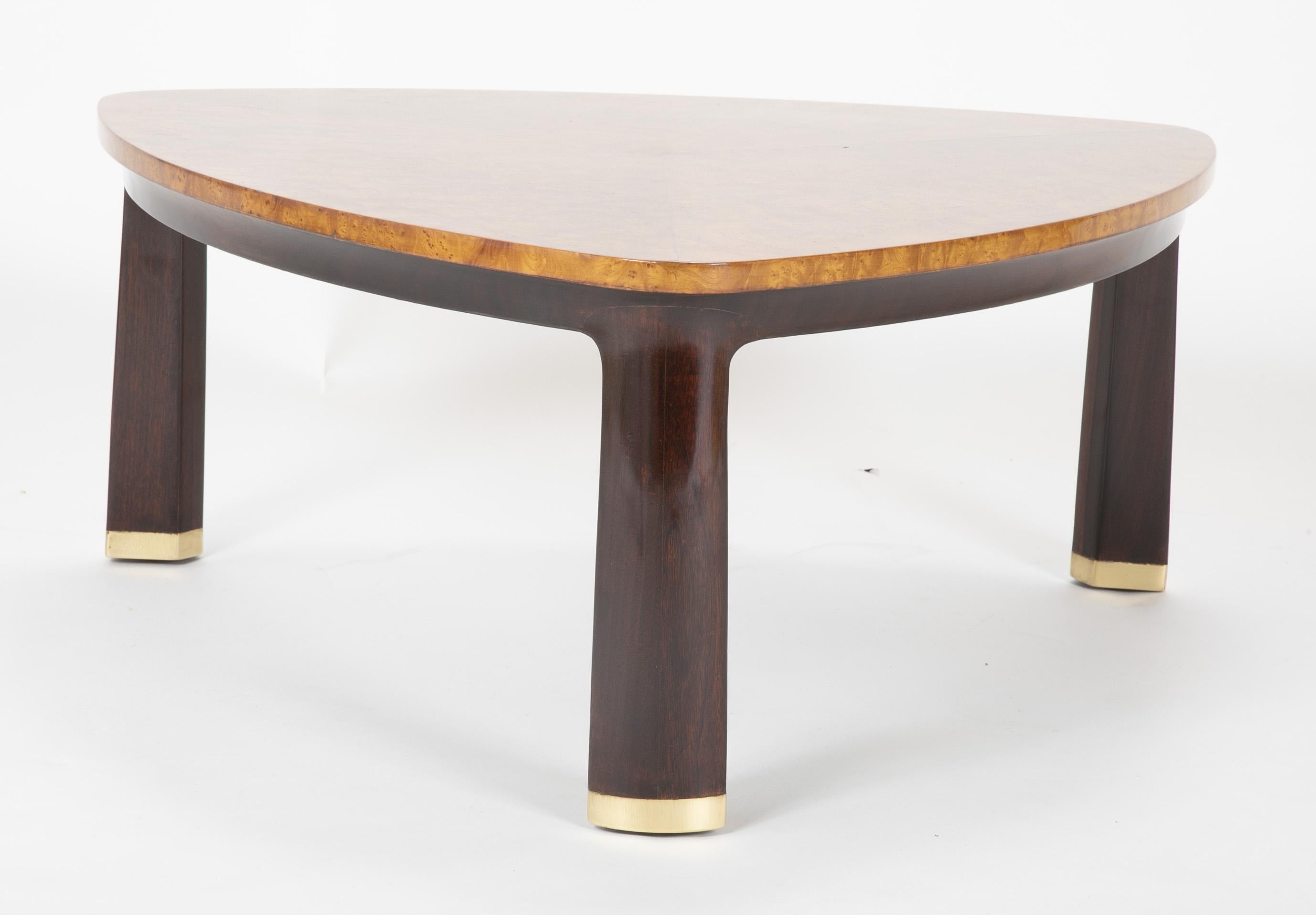 A burled triangular top coffee table rising from three walnut legs tipped with brass caps. Designed by Edward Wormley for Dunbar, circa 1955.