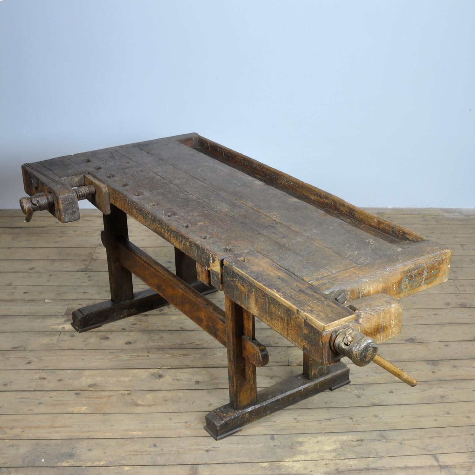 This antique workbench has two hand carved built-in wooden vice screws and a recessed tray where the carpenter would put his tools. It was manufactured around 1900. Made from oak. Beautiful patina after years of intensive use. The workbench has been