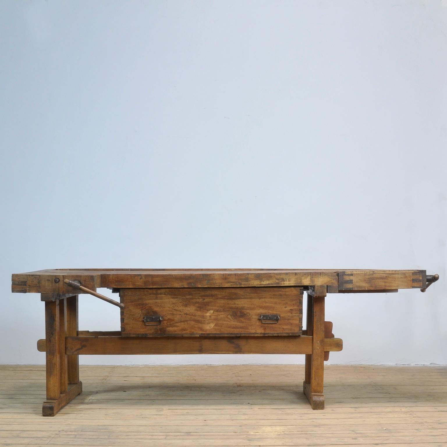 This antique workbench has two hand-carved built-in wooden vice screws and a recessed tray where the carpenter would put his tools. It was manufactured circa 1900. Made from oak. Beautiful patina after years of intensive use. The workbench has been