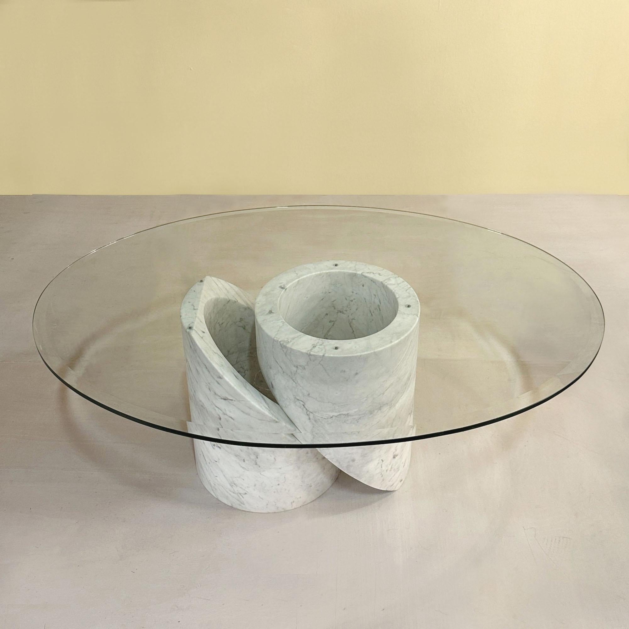 Mesa de centro escultórica de mármol de Carrara con tapa ovalada de cristal, Italia Años 60. La base está formada por dos cilindros de mármol entrelazados. La tapa ovalada de cristal tiene un ancho borde biselado y pulido.
Para el envío, la base