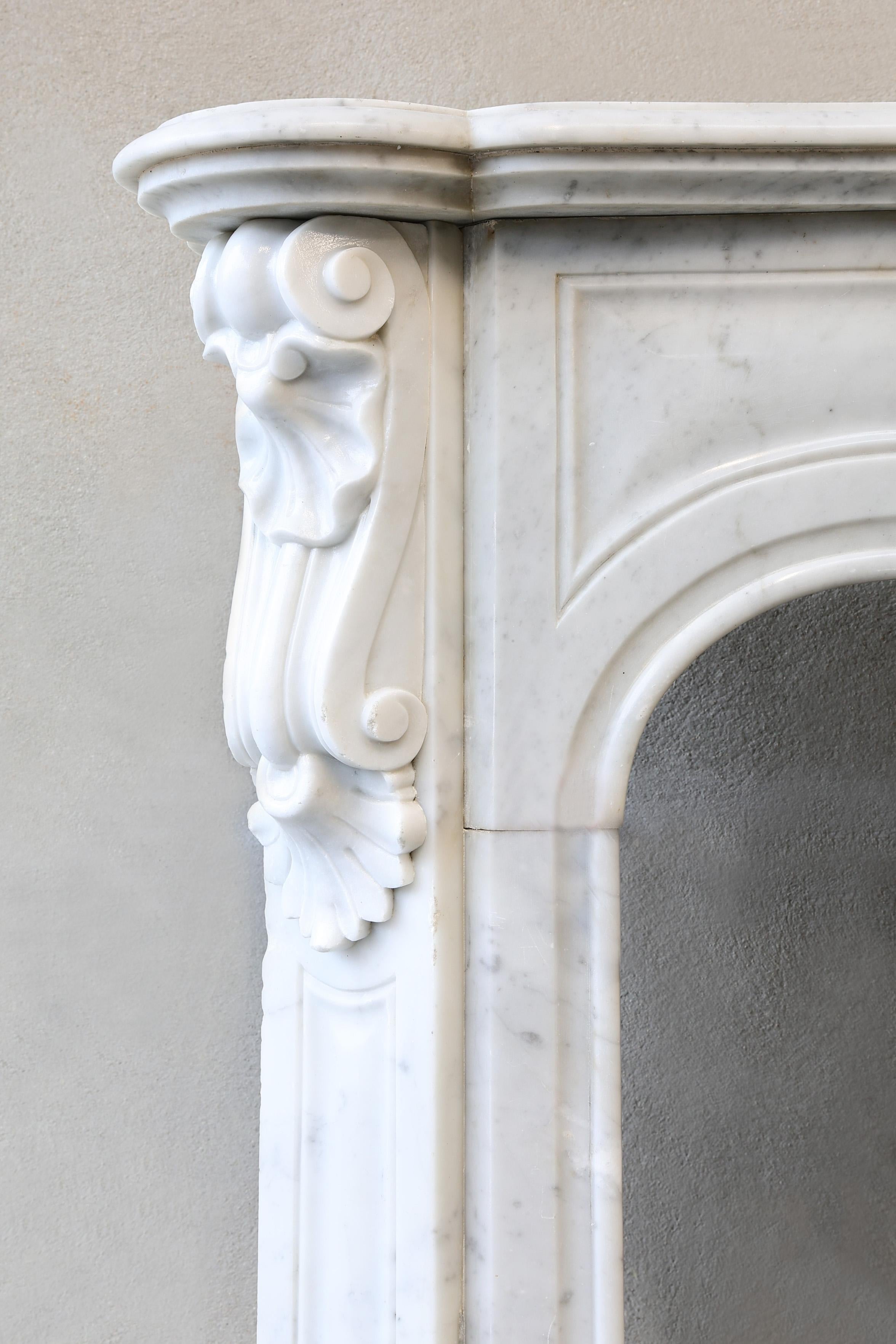 Beautiful antique Carrara marble fireplace from the 19th century in Pompadour style. This white marble fireplace has a beautiful ornament in the middle and graceful elements on the legs. A beautiful compact mantle surround that will fit well in many