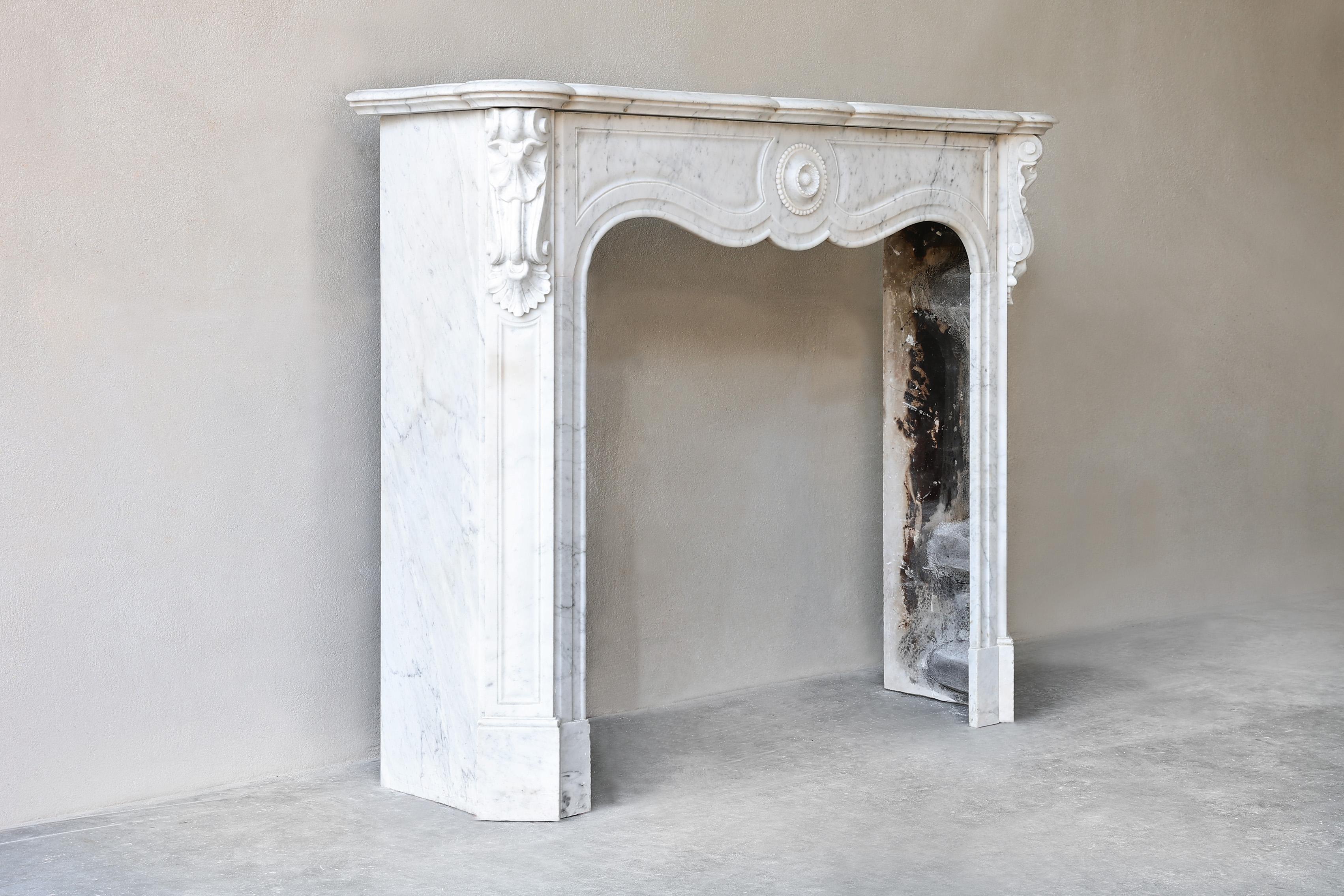 Beautiful antique fireplace from the 19th century in Pompadour style. A compact mantle due to its size with an elegant look and the various ornaments and decorations! This Carrara marble mantel is chic and adds value to your interior!
