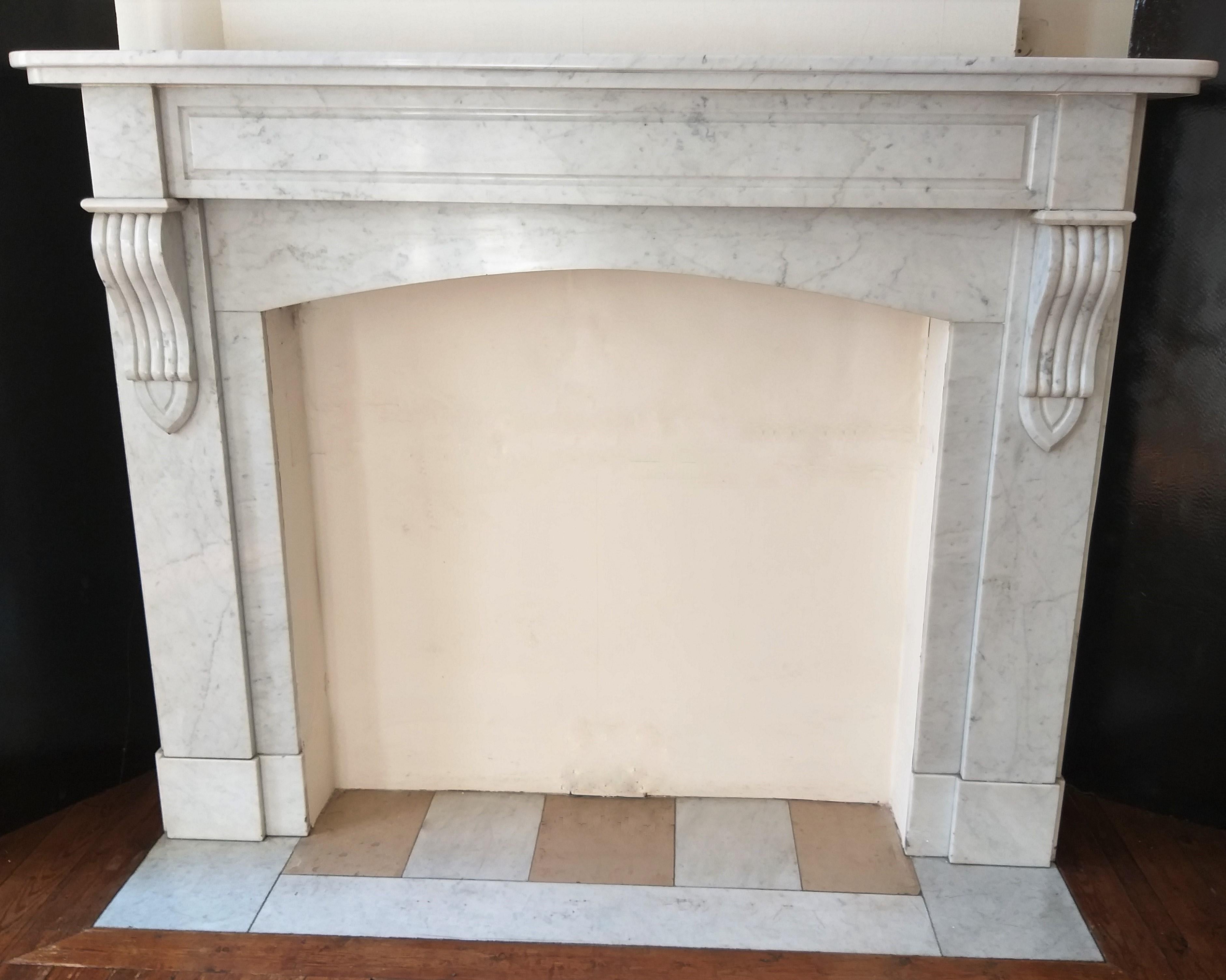 A simple and elegant Carrara marble fireplace. The two undulating corbels are supporting a broad moulded shelf.
Its' simplicity is in perfect harmony with the softly white-grey hued Carrara marble. This fireplace will be delivered with his original