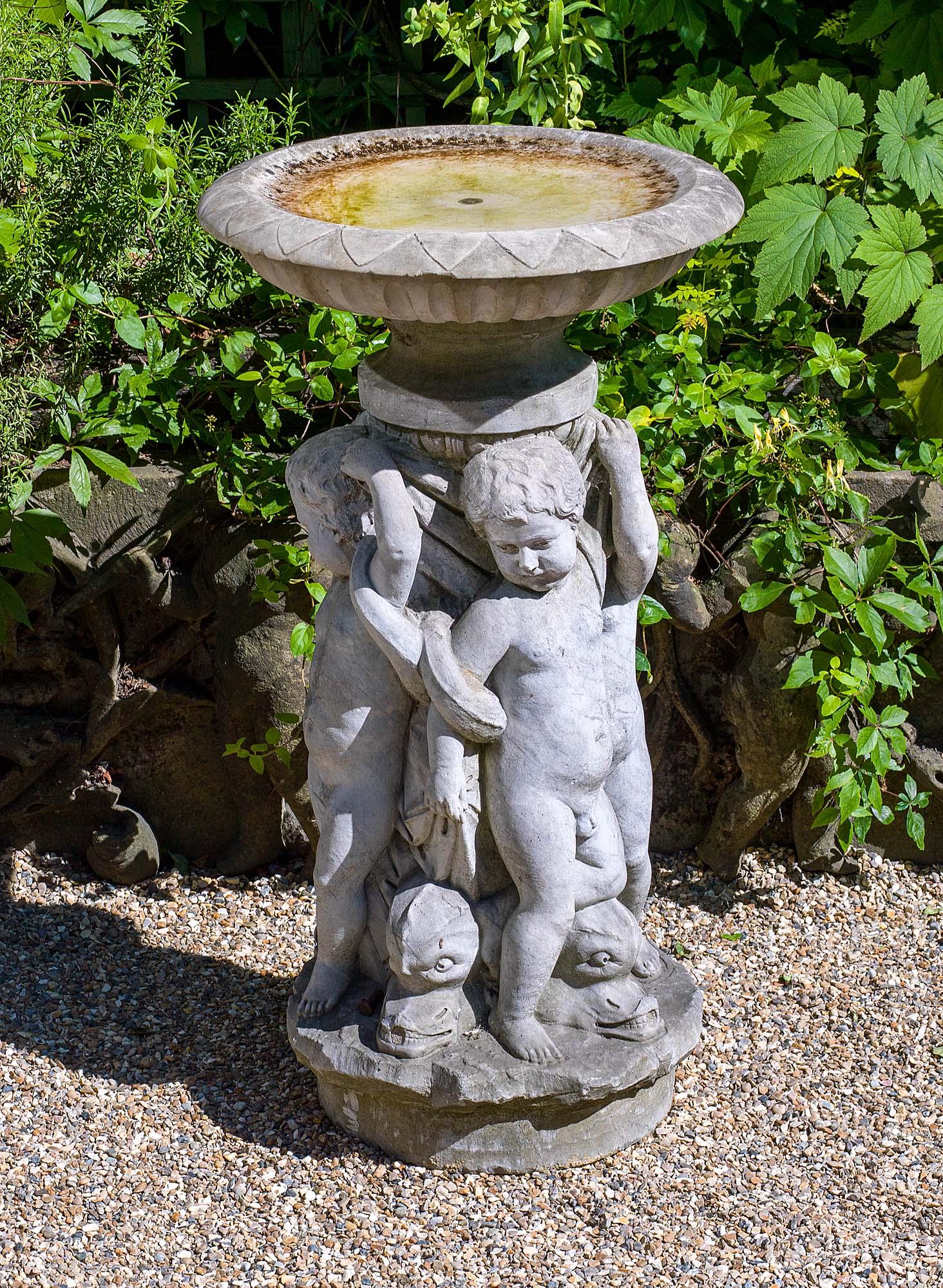A carved Carrara marble fountain centrepiece with four entwined putti holding a gadrooned bowl aloft standing astride stylised dolphins mounted on a rustic base.
Italian, mid-late 19th century.
  
