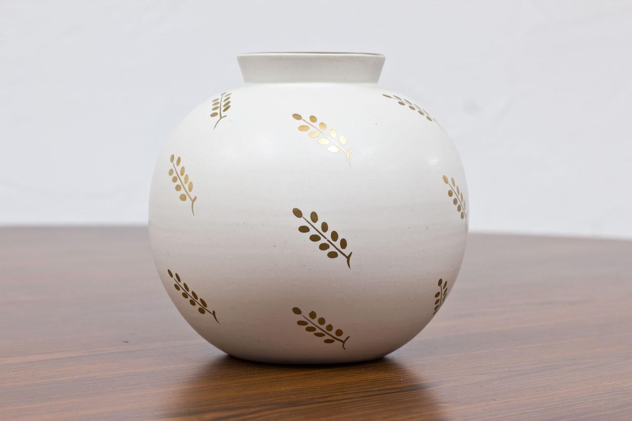 Graceful round vase designed by Wilhelm Kåge, manufactured at Gustavsberg in Sweden during the 1940s. Made from white Carrara glaze with gold-colored leave pattern. Model number 1042. 
Stamped on the bottom.

Condition: very good vintage condition