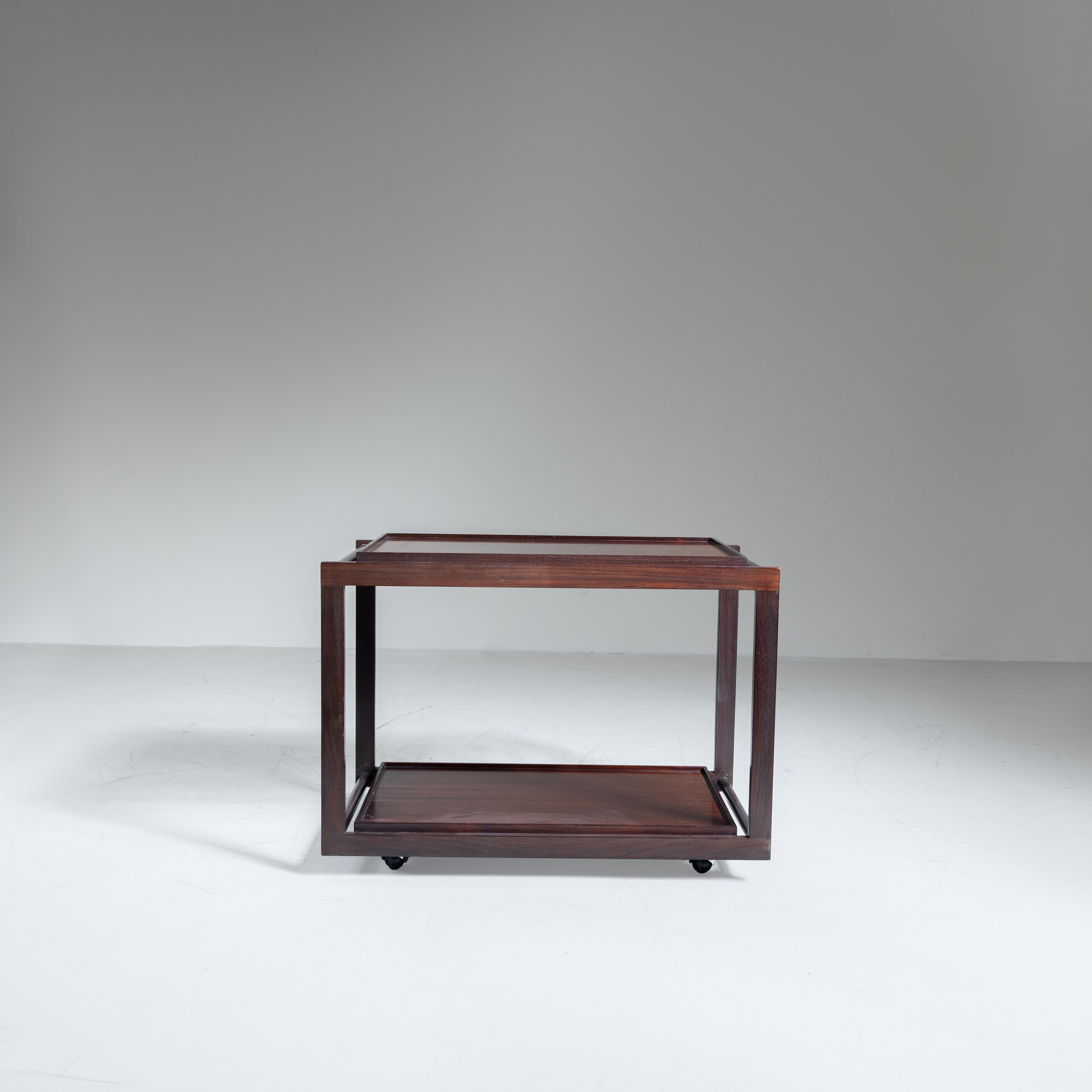 Chariot à roulettes avec deux plateaux amovibles, conçu par Gianfranco Frattini pour Cassina. Fabriquée en bois massif de haute qualité, cette table roulante allie fonctionnalité et élégance dans un design raffiné et intemporel. Les deux plateaux