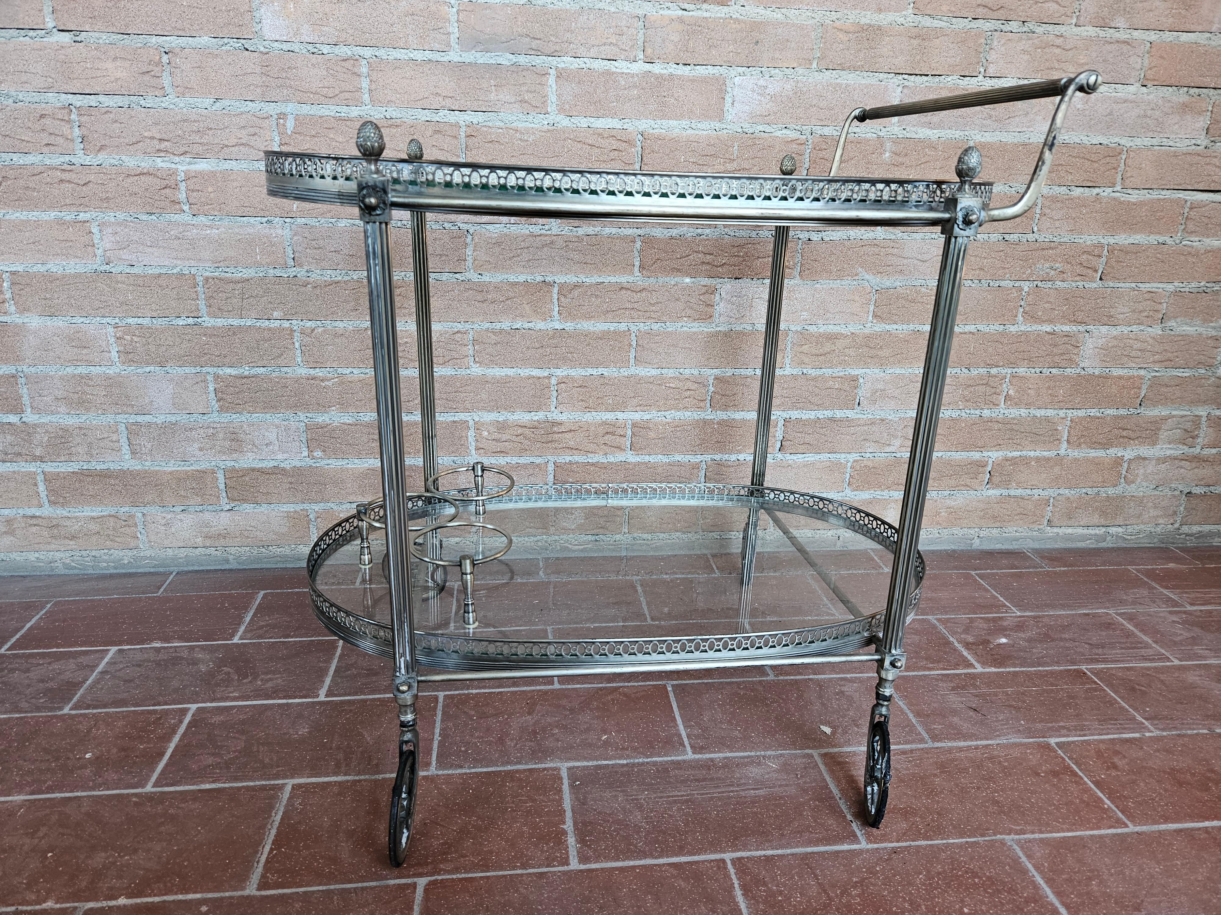 Brass bar cart with double glass shelf and various workings along edges and main structure.

It has a handle and four large wheels for easy movement in rooms such as living rooms or kitchens.
Also of note are the bottle compartments.

Normal signs