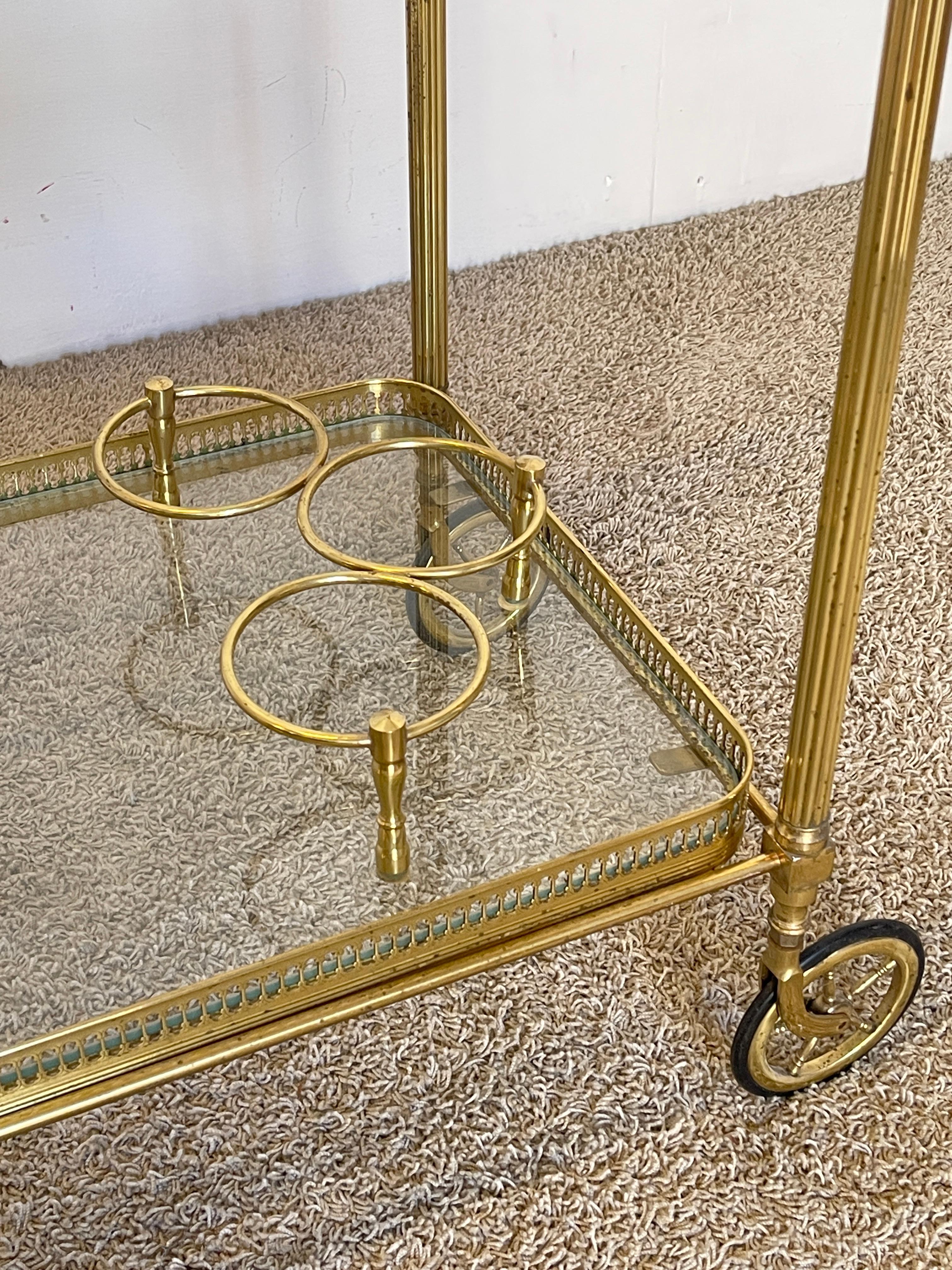 Carrello bar vintage in ottone dorato con doppio ripiano in vetro e vassoio superiore estraibile, perfetto per servire con stile. Le finiture dettagliate, la ringhiera decorativa e le ruote originali lo rendono un pezzo d'arredo unico, ideale per