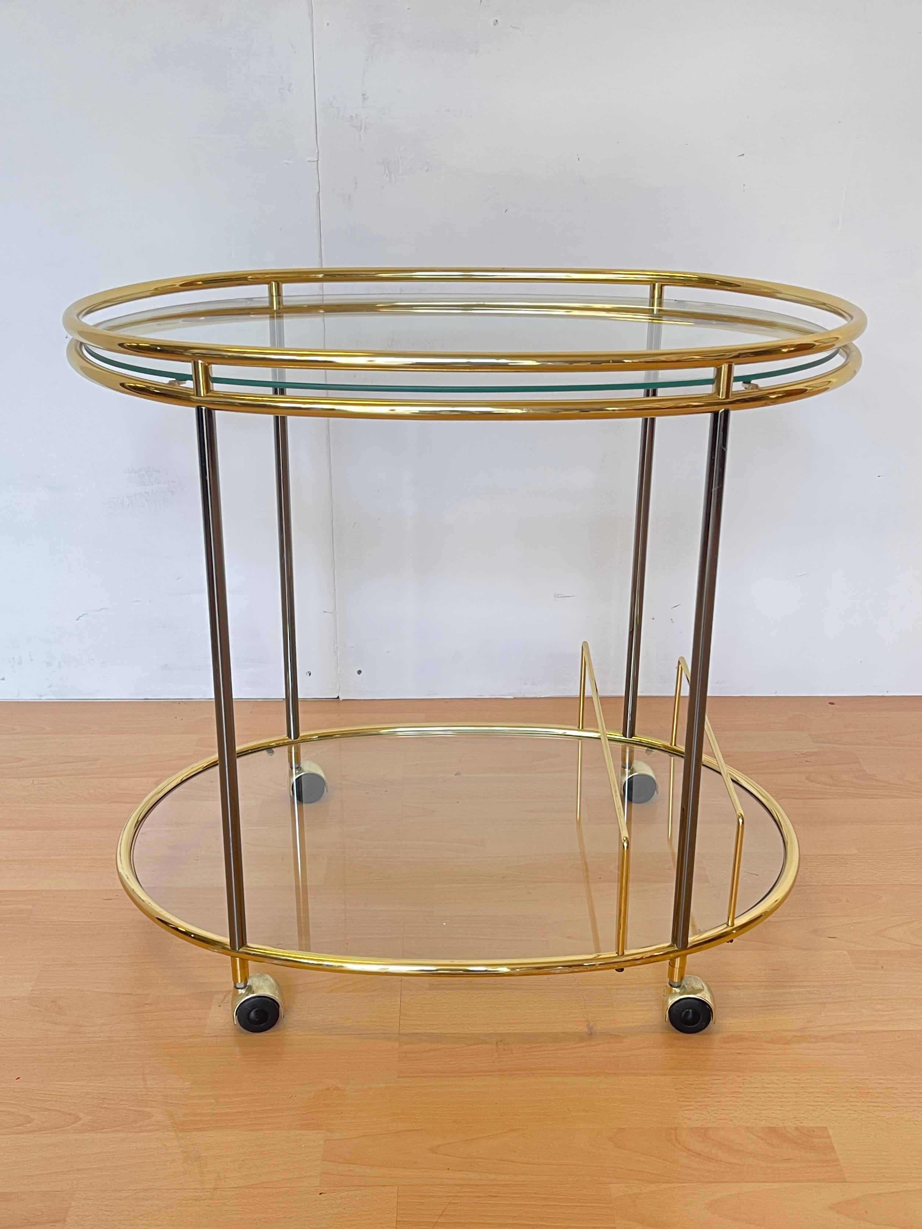 Raffiné et fonctionnel, ce chariot de bar de style Mid-Century est un véritable joyau de la décoration intérieure. La structure ovale en laiton doré accueille deux étagères en verre transparent, offrant espace et luminosité. Les lignes épurées