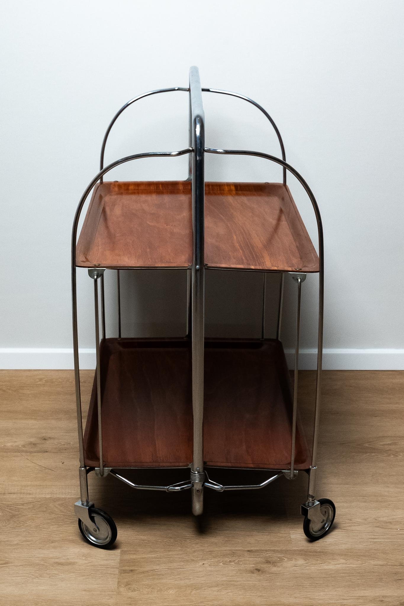 Carrito de bar o de comida de plástico y metal cromado, Alemania, años 60. 
Carro plegable para bar o comida en laminado plástico marrón / metal cromado. El carro tiene cuatro ruedas. 
Todo es ORIGINAL y conserva la pátina del tiempo. 
Puede mostrar