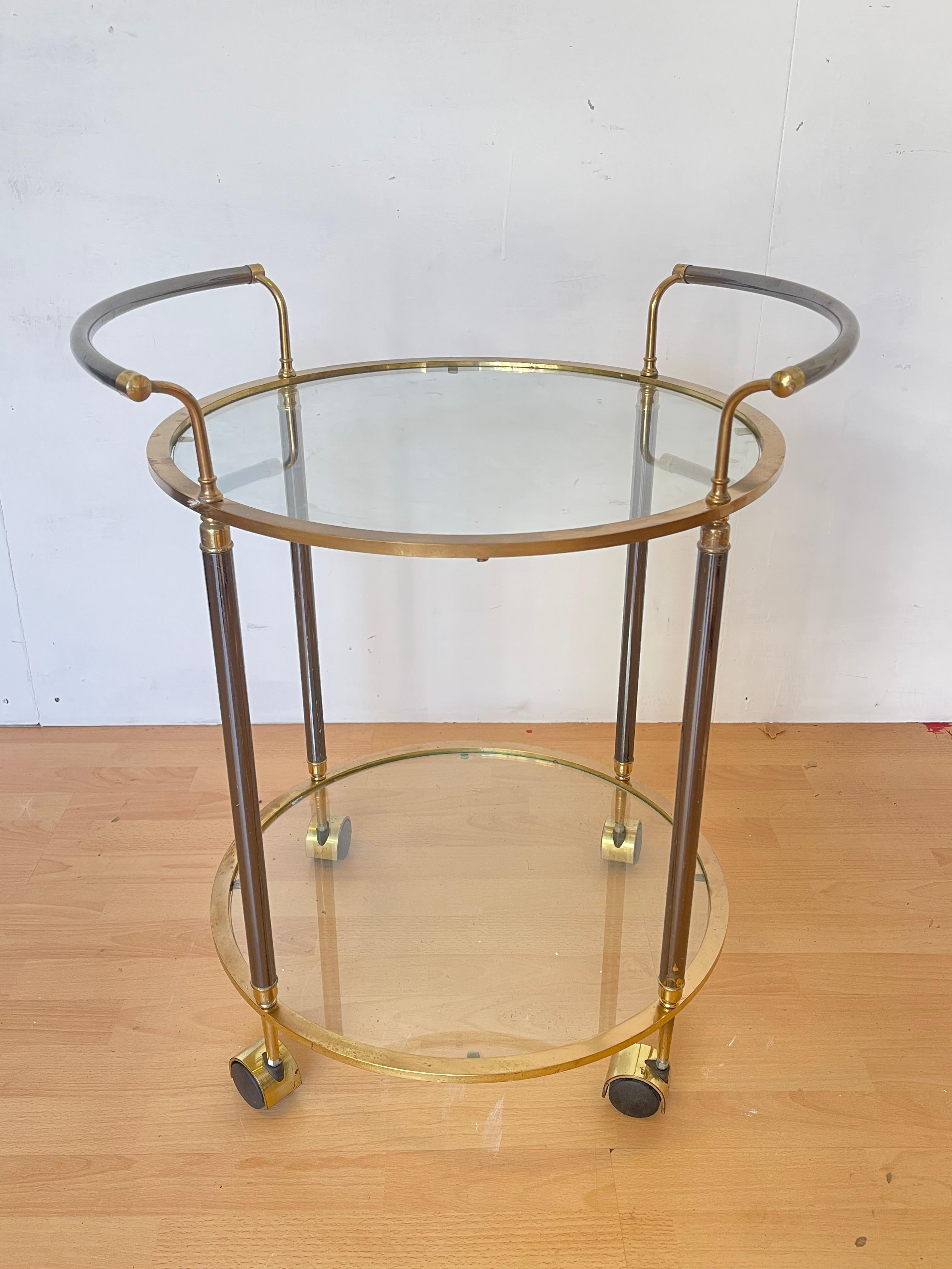 Elégant chariot de bar vintage fabriqué dans les années 1960, avec une structure en laiton et en verre. Le design raffiné comprend deux étagères rondes en verre transparent, encadrées par des détails en laiton poli et soutenues par des montants