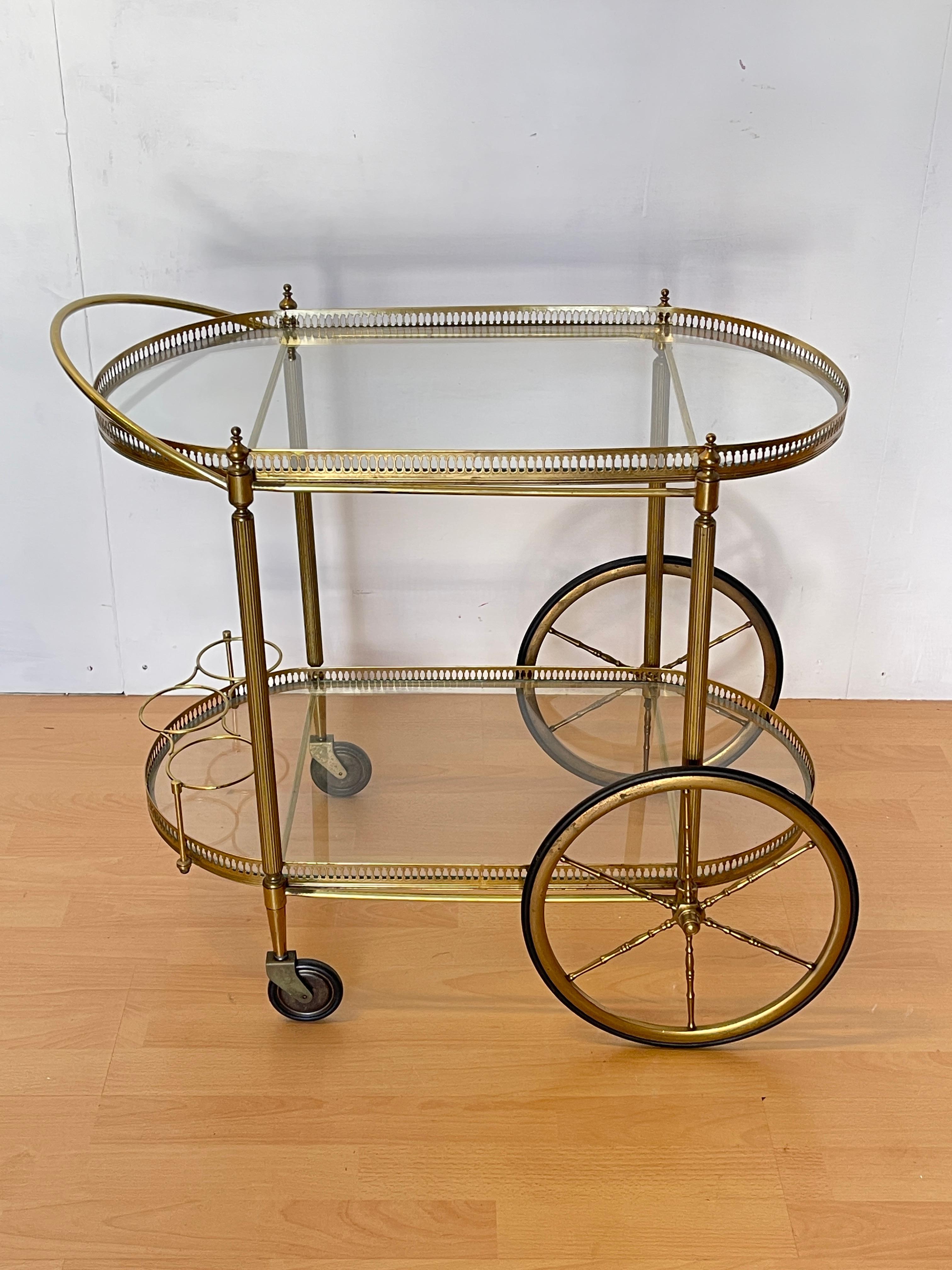 Chariot de bar vintage raffiné de style hollywoodien des années 1960, un meuble emblématique qui allie classe et fonctionnalité.
Le cadre en laiton doré avec ses détails décoratifs ajourés apporte une touche de luxe intemporel, tandis que les