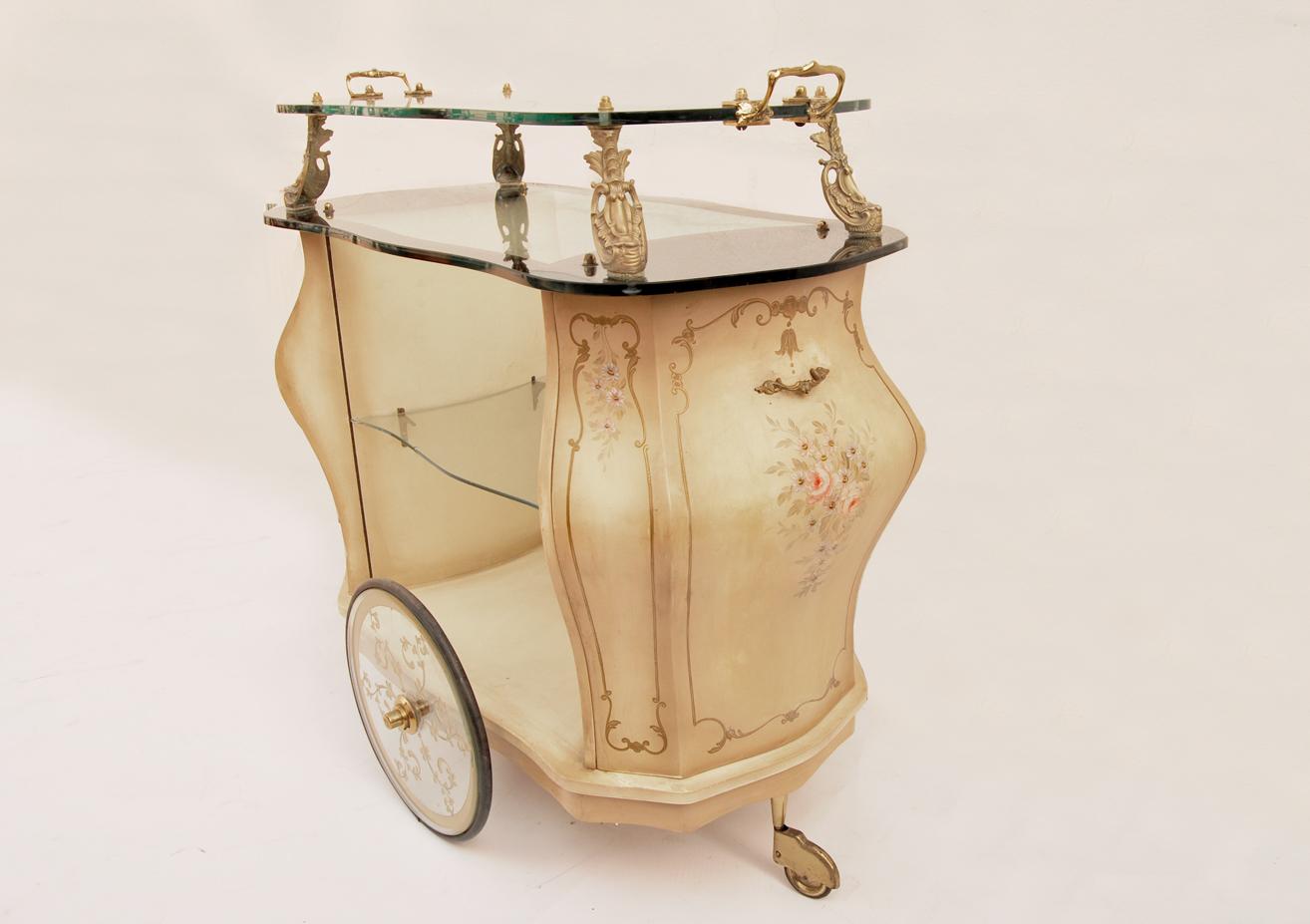 Beautiful vintage bar cart dating from 1960. 
This item, made in Italy, is made of wood, glass and brass.
The wooden frame is decorated with flowers and frames reminiscent of the Venetian style. The top glass and that of the wheels, transparent, 
