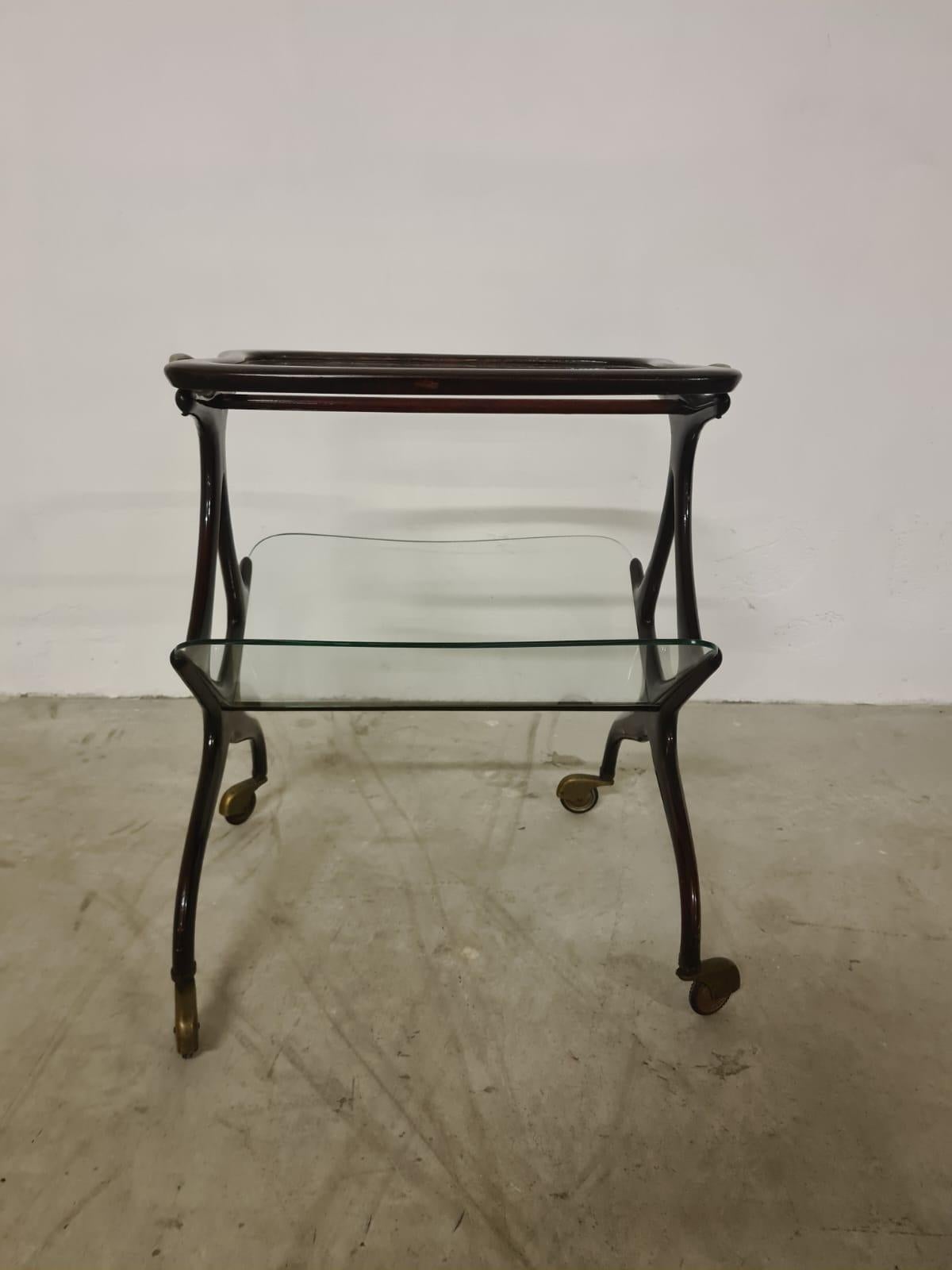 Trolley mit Zeitschriftenständer von Cesare Lacca.

Raffinierter Wagen mit geschwungenem, weich gebeiztem Walnussholzrahmen, Messingdetails und geschliffenen Glasböden.

Im unteren Bereich befinden sich zwei V-förmige Glasböden, die als