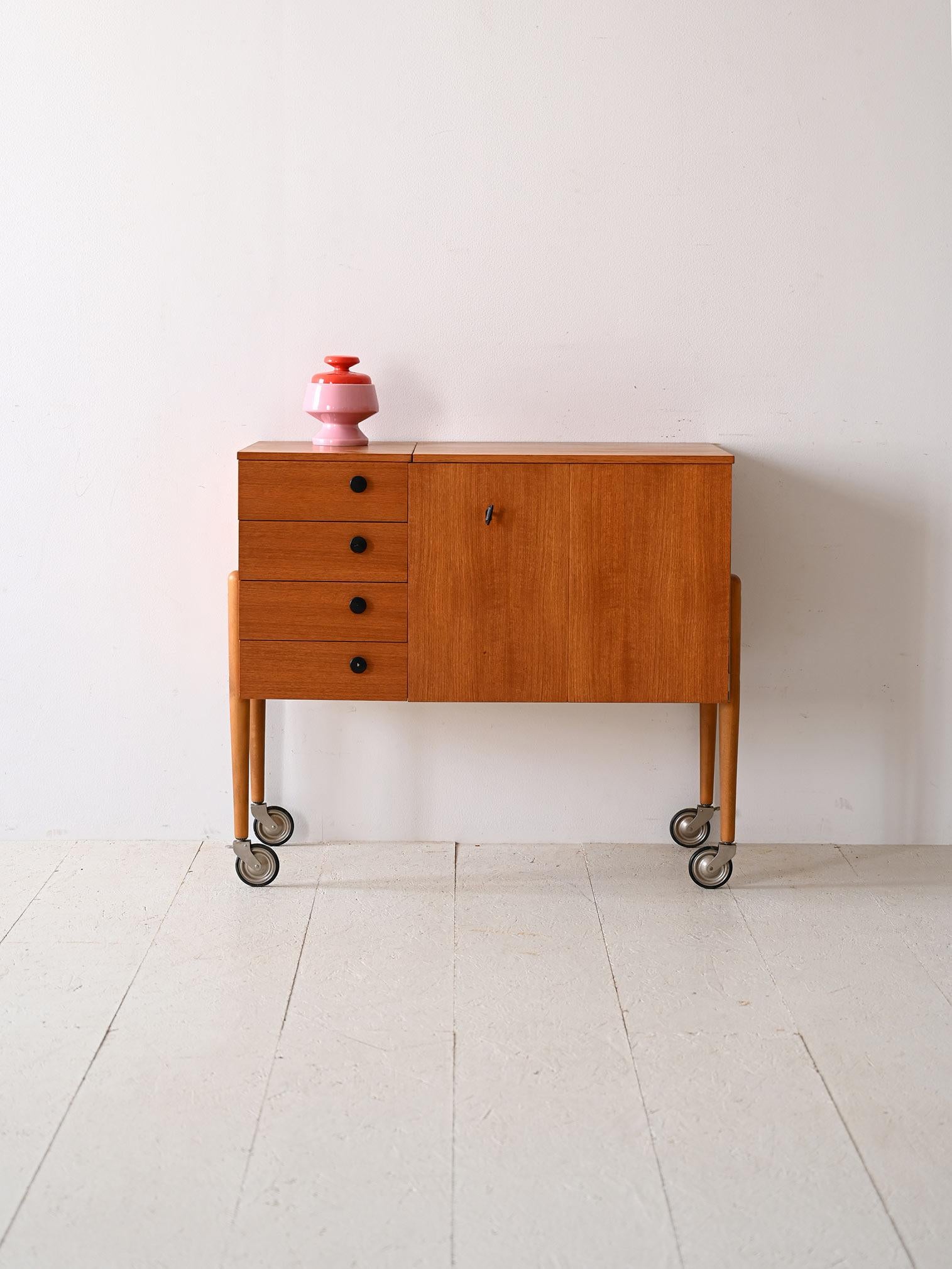 Scandinavian cabinet on wheels from the 1960s.

The teak frame and practical drawers make it a perfect example of functional design. Tapered legs ending in metal and rubber wheels , add a detail of style and practicality. 
The drawers have black