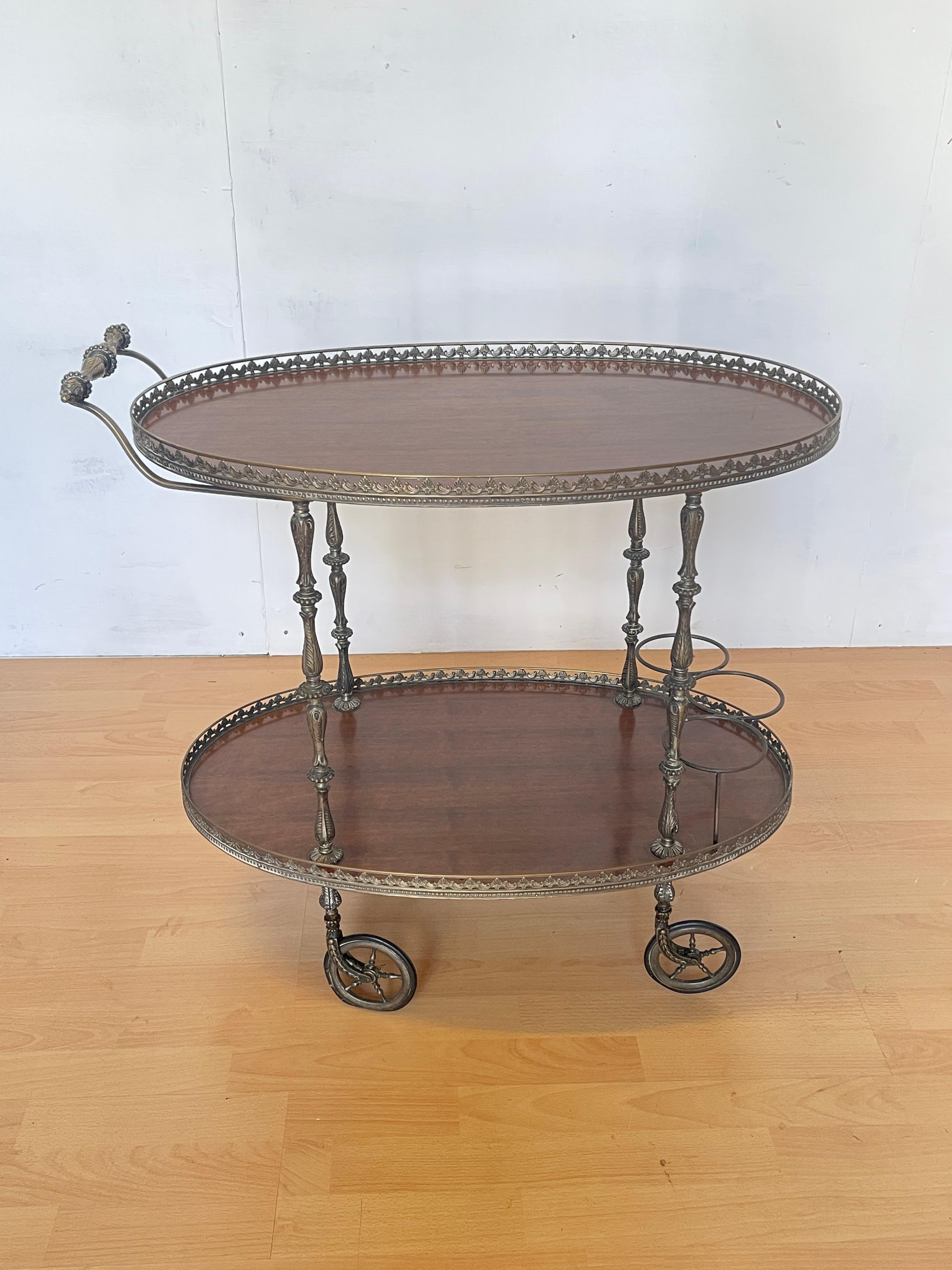 Élégant chariot de service vintage de style classique, doté d'un cadre en laiton finement travaillé et d'étagères en bois poli de couleur noyer. Le décor en relief, les pieds tournés et la forme ovale font de cette pièce un exemple authentique de