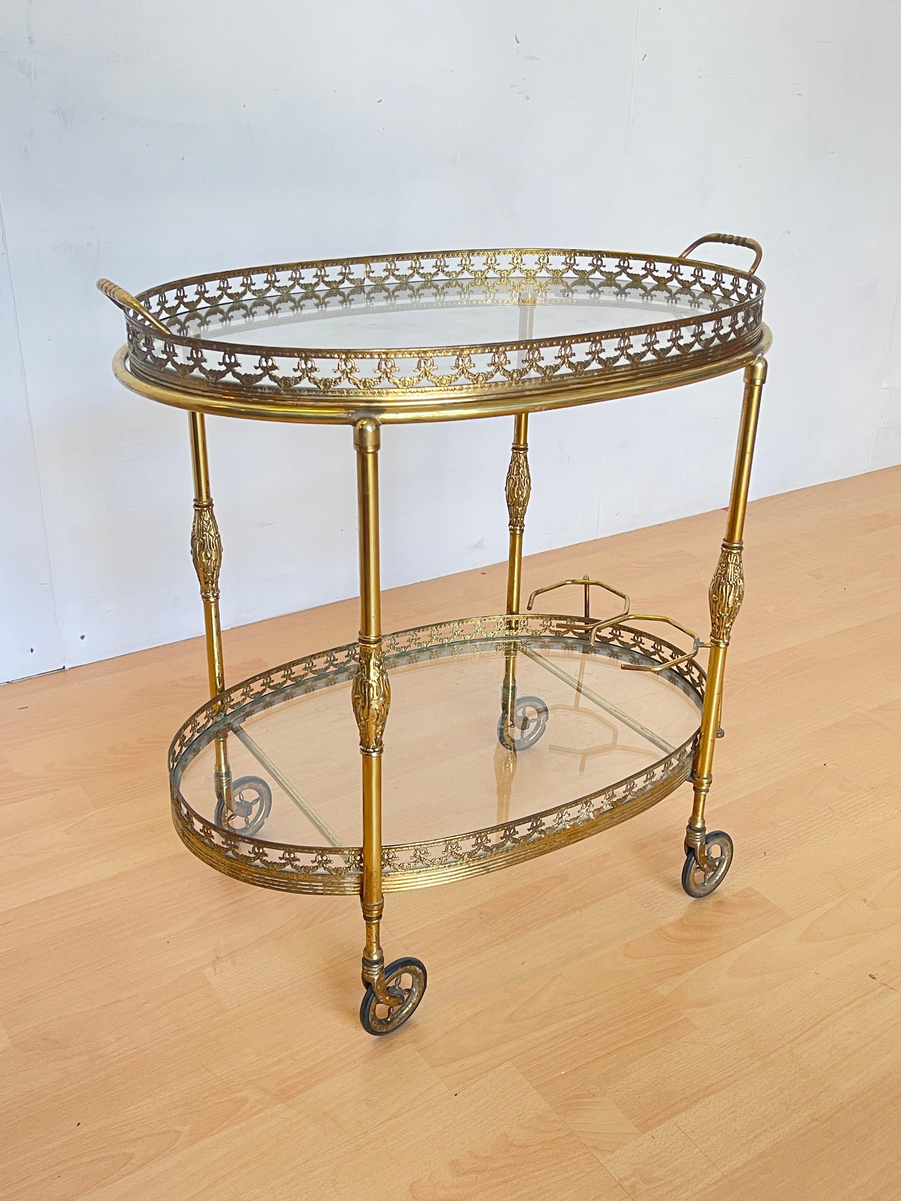 Elégante table roulante vintage pour le thé ou le bar en laiton doré avec étagères en verre, datant du milieu du 20e siècle. Le design raffiné de style baroque français est agrémenté de détails ornementaux et de reliefs sur l'ensemble de la