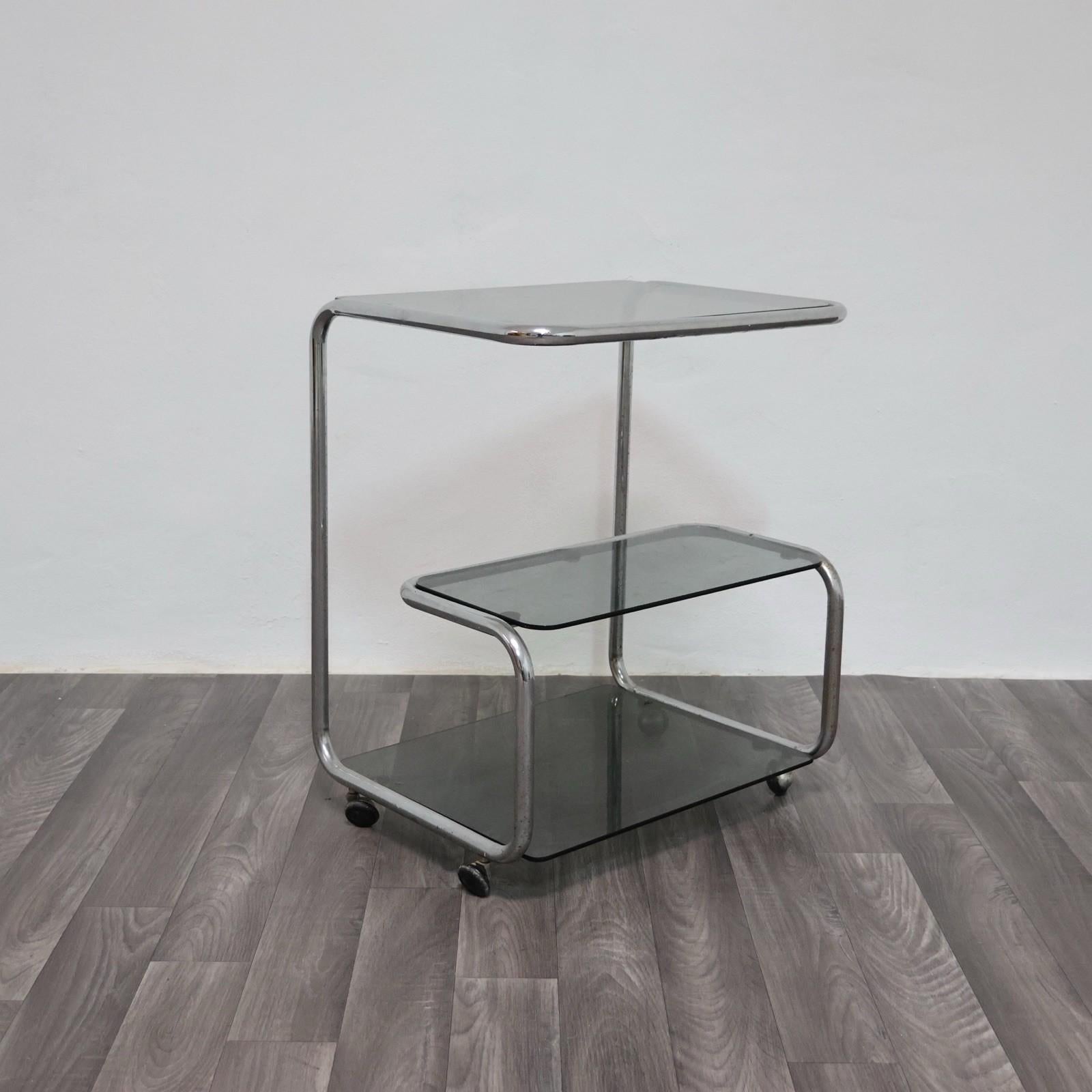 Elegante carrello portavivande degli anni ’70, realizzato in acciaio cromato con tre ripiani in vetro fumé. Il design sinuoso e minimale richiama lo stile modernista tipico del periodo, con struttura tubolare continua e angoli morbidi che