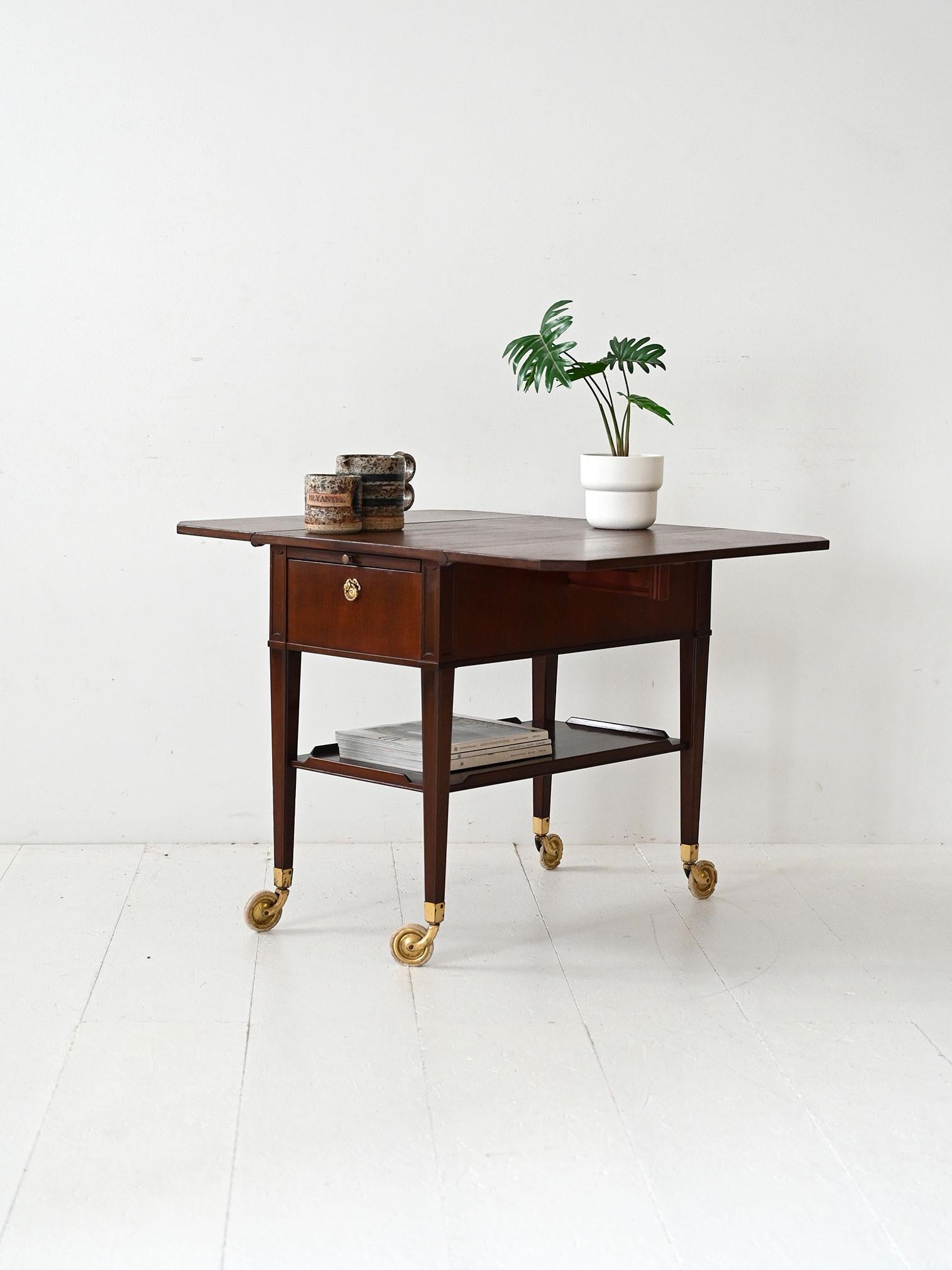 Carrello scandinavo anni 40 in mogano con due cassetti, ali laterali apribili e dettagli in ottone.

Carrello scandinavo vintage degli anni 40 realizzato in mogano con dettagli in ottone. Dispone di due cassetti frontali con maniglie originali, ali