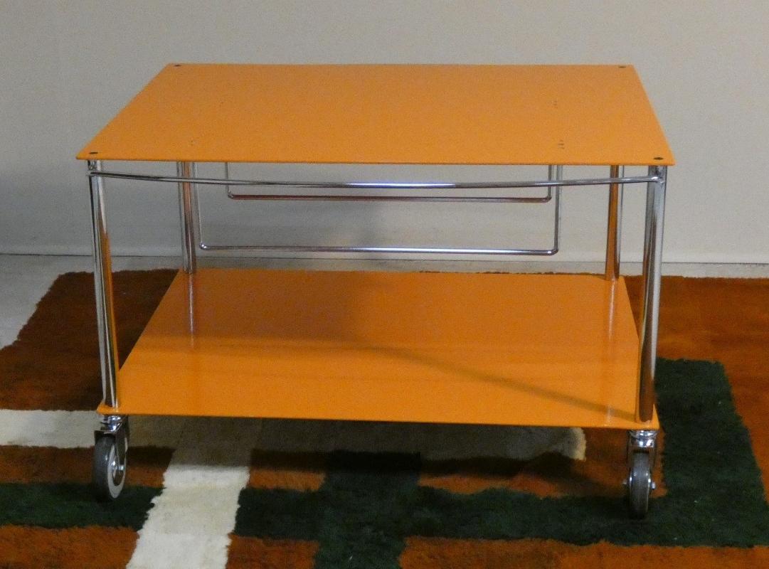 In un meraviglioso colore arancione, il carrello portatelevisore Trolley TY (precussore del Moby 2) disegnato da Marco Zanuso e prodotto da De Padova. Il design è contemporaneo ed essenziale, con una struttura massiccia e stabile.  Le gambe in