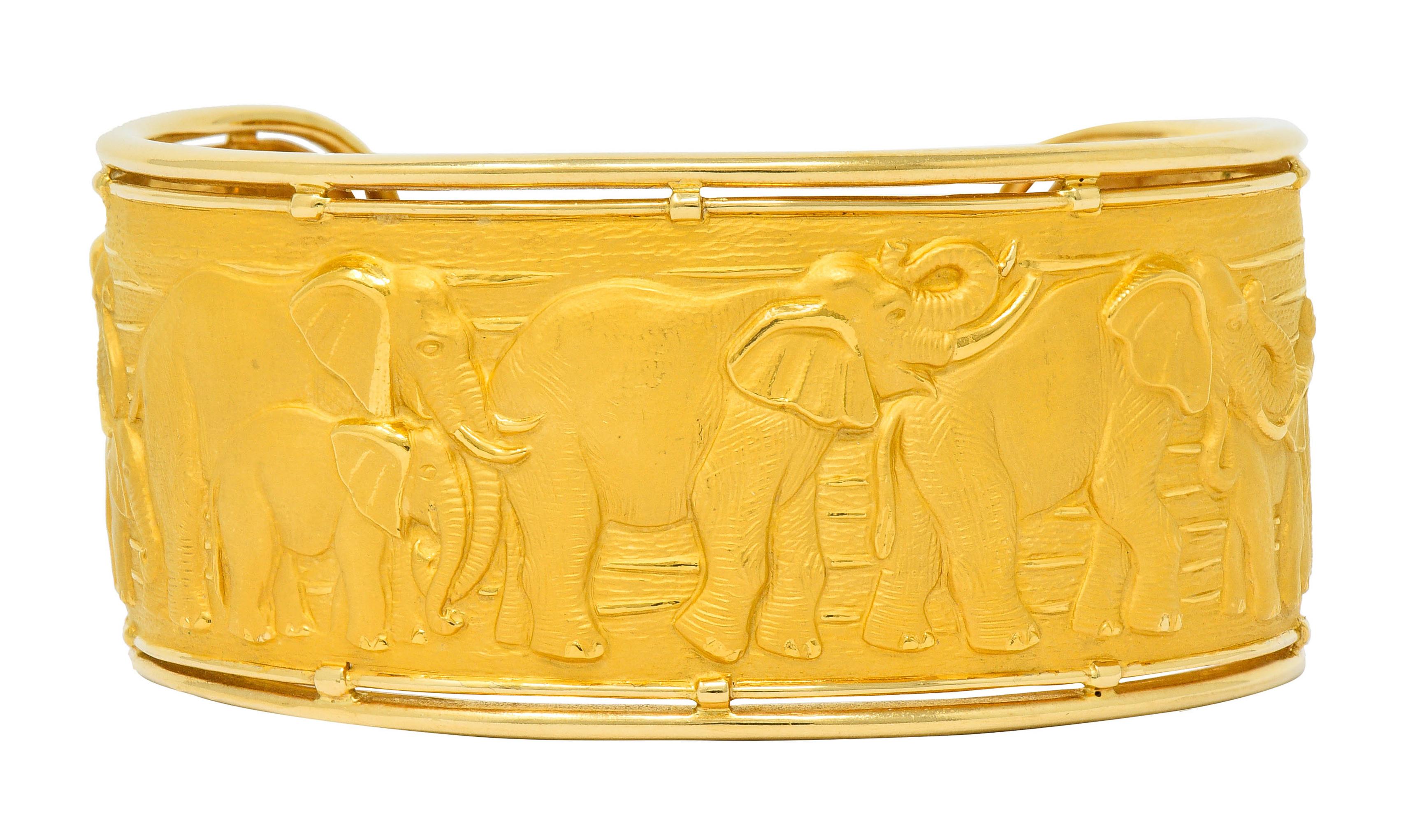 Wide cuff bracelet featuring polished edges contrasting highly rendered repoussè

Depicting a family of traversing elephants with high polished details against finely textured matte gold

Stamped 750 for 18 karat gold

Numbered with maker's mark for