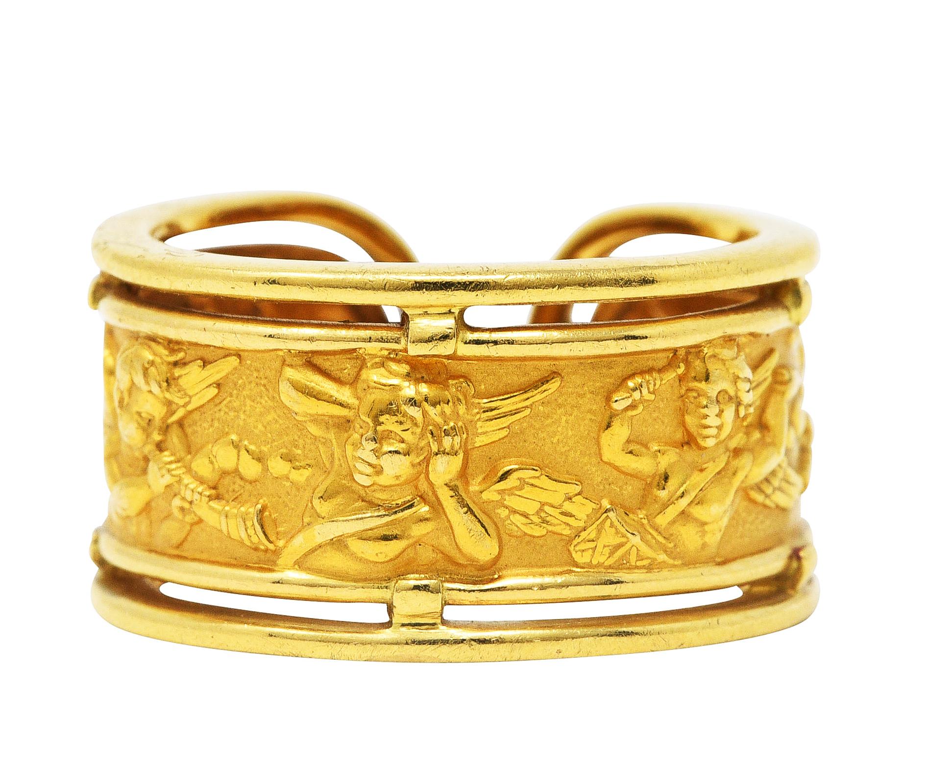 Band ring designed as cuff shape with central panel depicting repoussé cherubs

Cherubs are depicted joyously playing various instruments

With gold frame surround

Stamped 750 for 18 karat gold

With maker's mark for Carrera y Carrera

From the