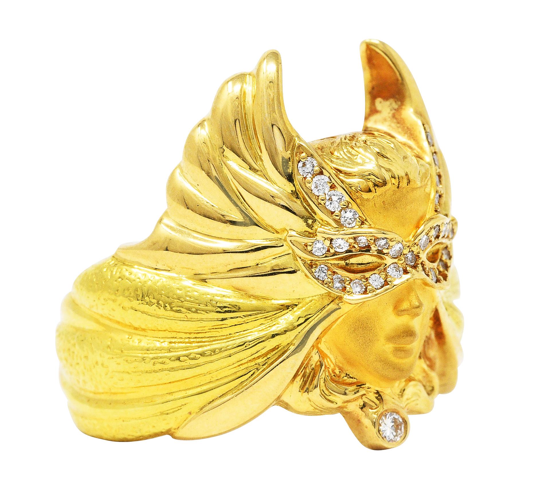 Ring designed as head of a woman wearing masquerade style mask with sweeping wings

Wings are grooved highly polished yellow gold with stippled green gold segments

Mask and collar are accented by round brilliant cut diamonds

Weighing approximately