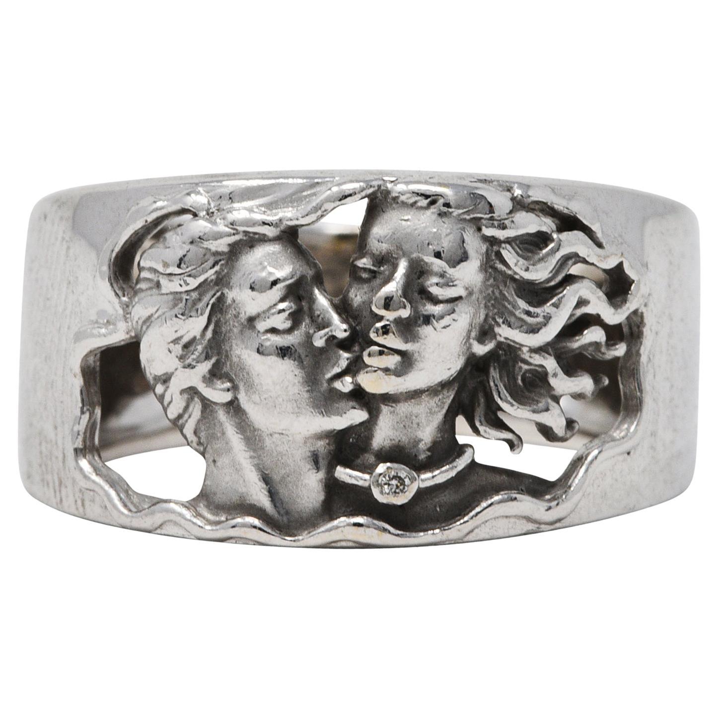 Wide band ring is pierced to front with a depiction of Adam affectionately kissing Eve

Highly rendered with a round brilliant cut diamond accent

Tested as 18 karat gold

Numbered with maker's mark

From the contemporary Adam & Eve collection

Ring