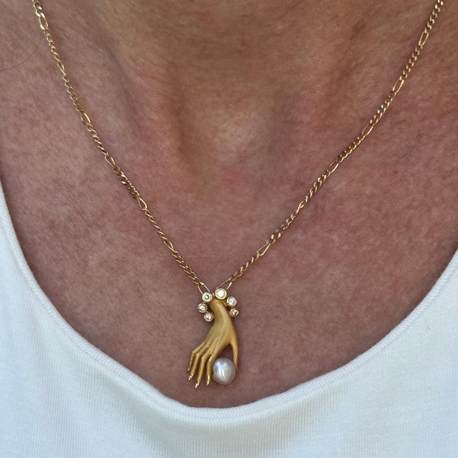 This striking 18k yellow gold necklace by Carrera y Carrera features the iconic Las Manos pendant—an intricately sculpted hand delicately cradling a luminous pearl. Accented with six round brilliant cut diamonds totaling approximately 0.10 carats,