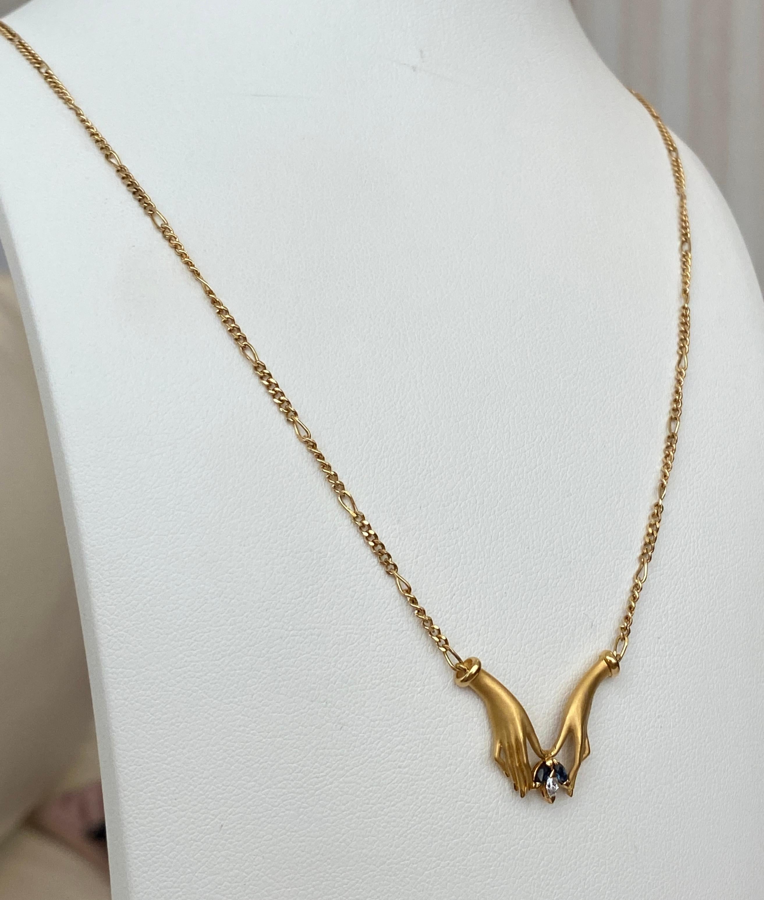 Angebotene Halskette aus 18 kt Gelbgold der Marke Carrera y Carrera. Der Anhänger mit Handmotiv ist mit einem Diamanten im Marquise-Schliff (ca. 0,05 ct G/VS) und zwei Saphiren im Marquise-Schliff (insgesamt 0,10 ct) besetzt. Die Halskette ist