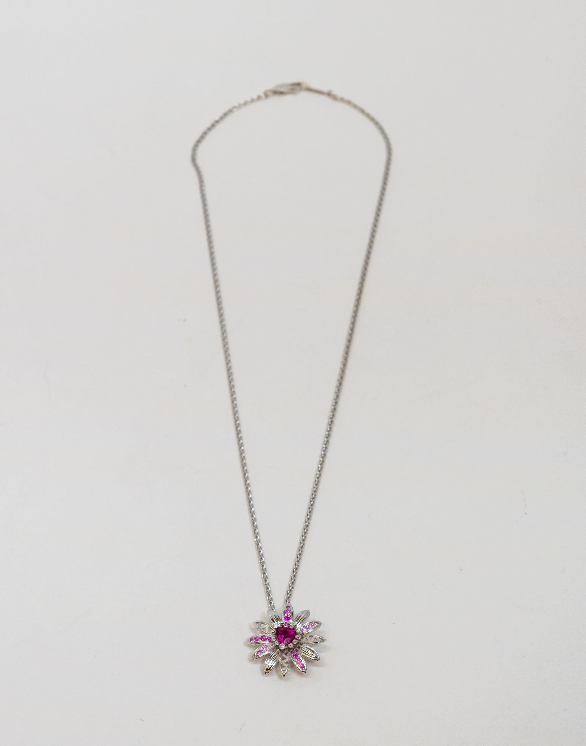 18K White Gold pendant. 18K White Gold cable chain with lobster claw lock. This piece has a flower-shaped pendant which decorated with a pink Sapphire main stone, 3 Diamonds, and 20 small light pink and pink Sapphires on petals.

Chain Length: 22