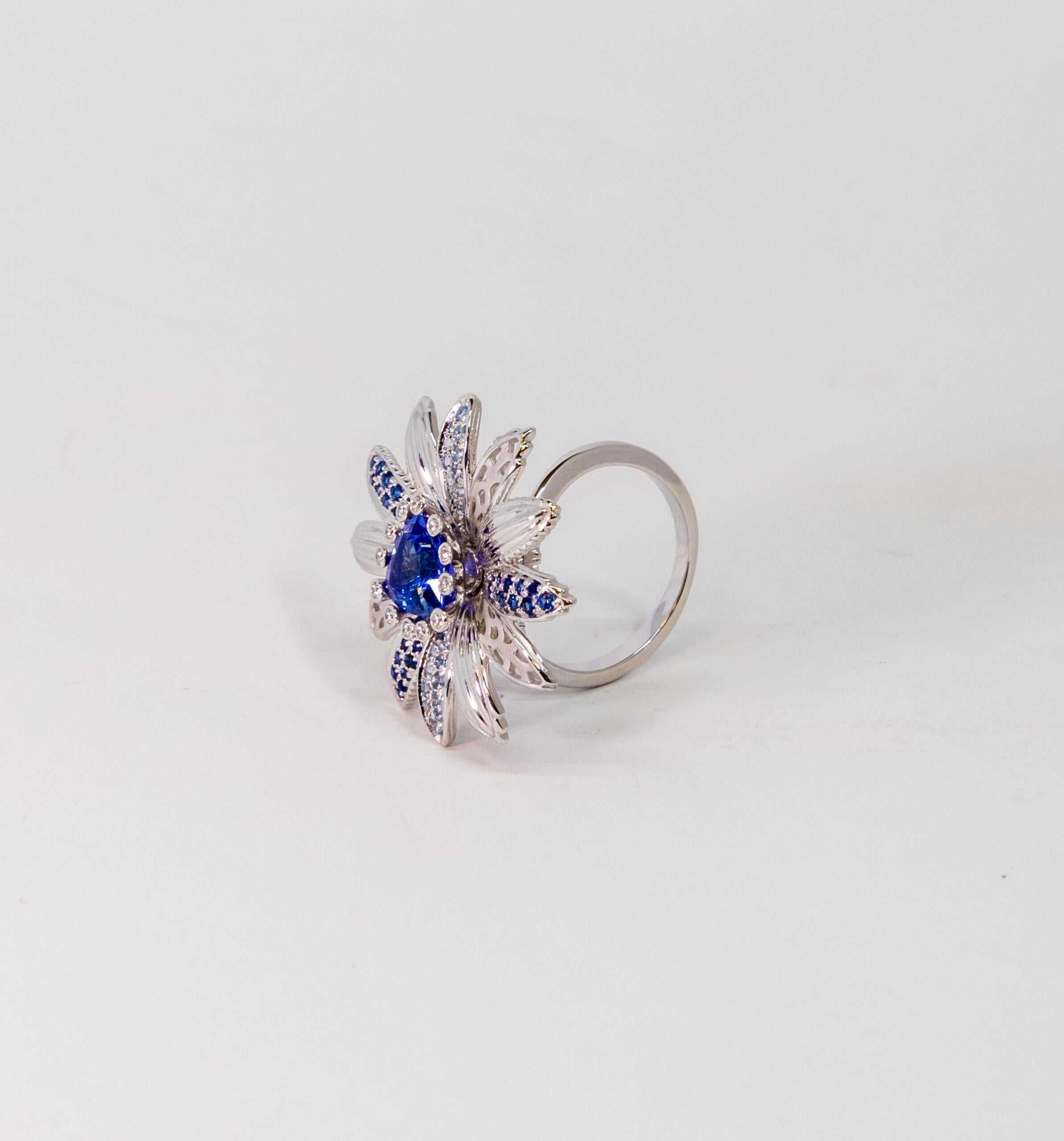 10070335 Carrera y Carrera  
This ring is made of 18K White Gold. The flower-shaped front side is decorated with triangle-cut main Blue Sapphire stone and light blue and dark blue side stones on petals totaling ~2.06ct. Main stone is surrounded by