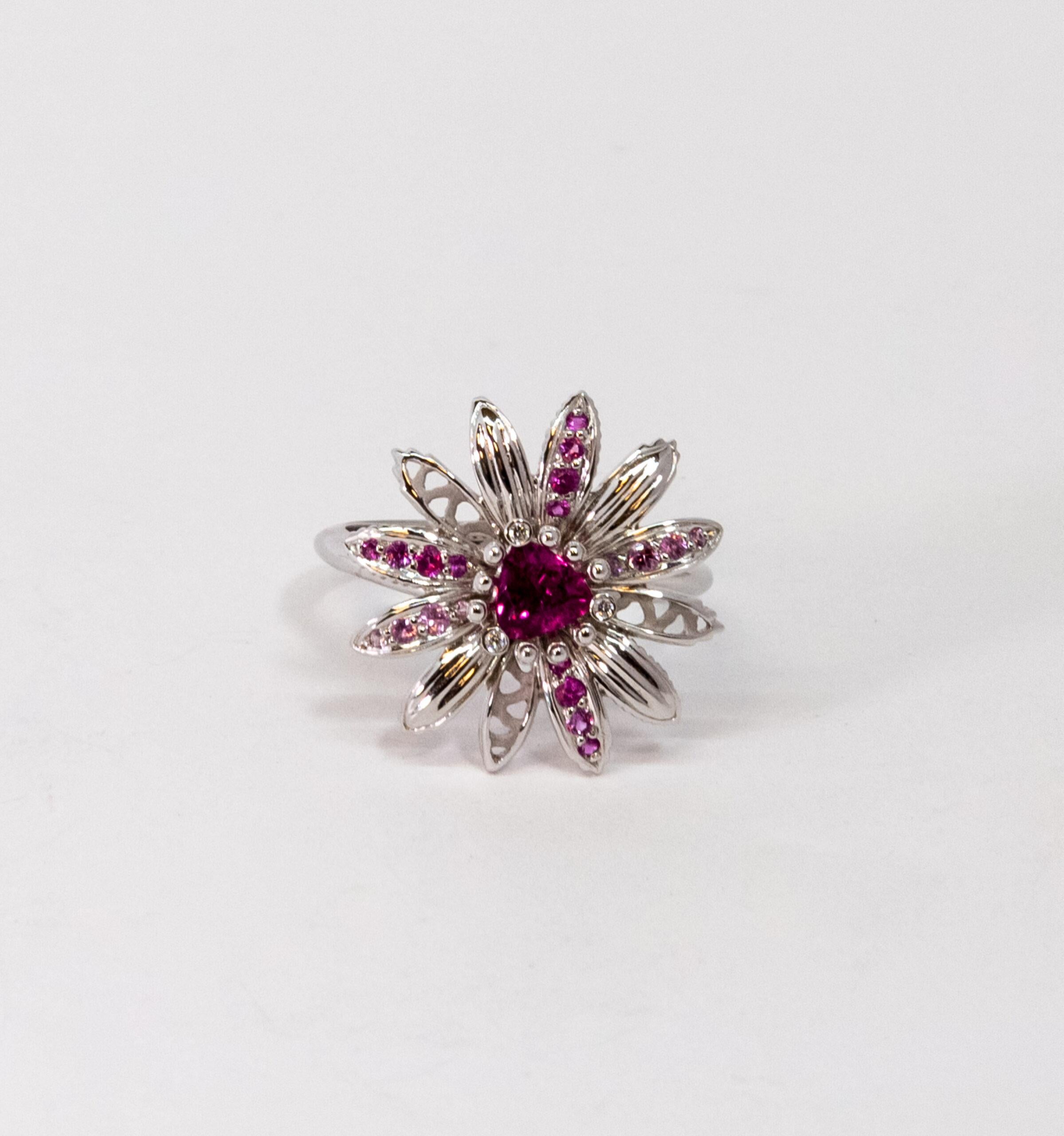 10070190 Carrera y Carrera  
This ring is made of 18K White Gold. The flower-shaped front side is decorated with triangle-cut main Pink Sapphire stone and light pink and dark pink side stones on petals totaling ~0.38ct. Main stone is surrounded by